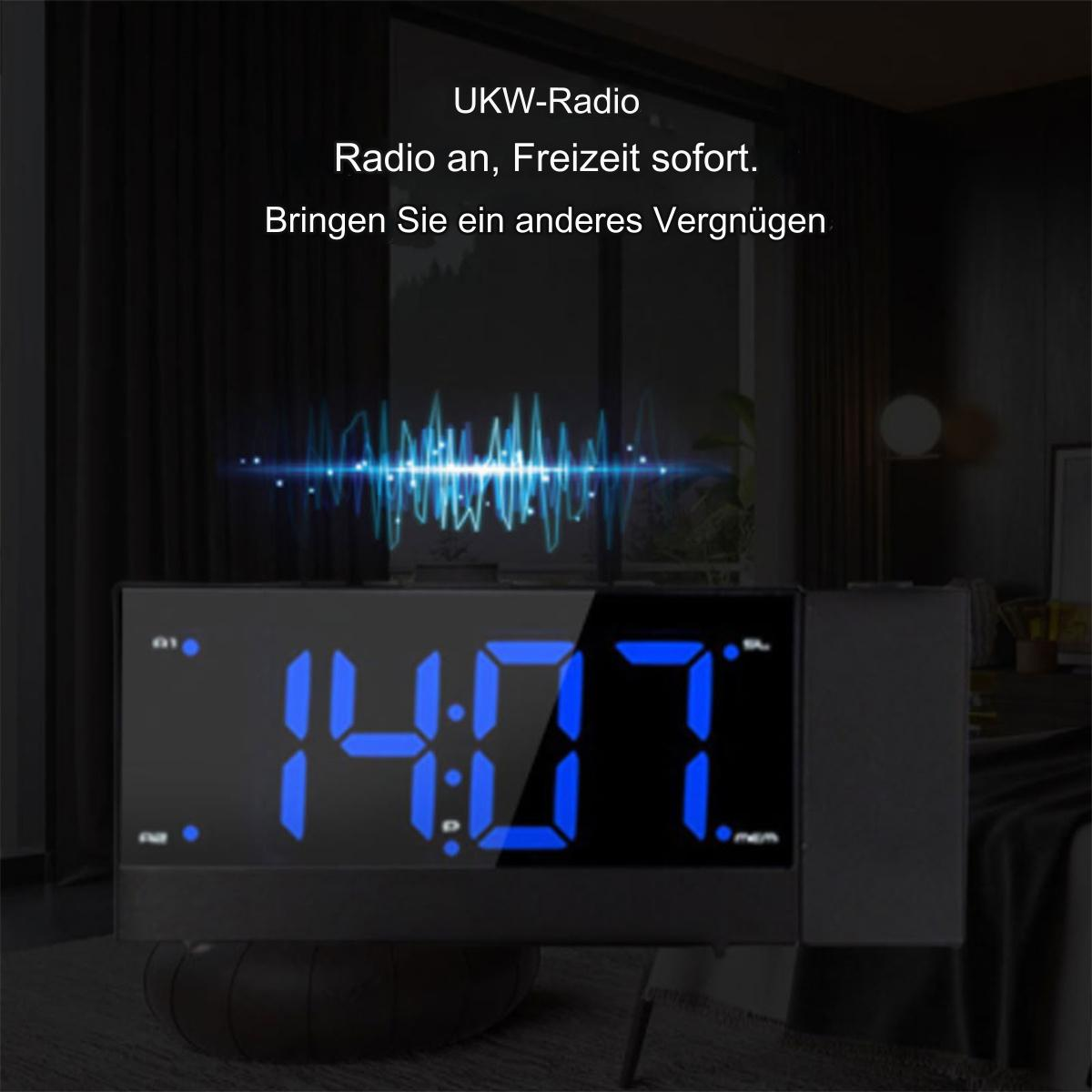Eine schwarze Digitaluhr, die blaue Zahlen anzeigt. Der Hintergrund ist ein Raum mit einem Bett und einem dunklen Vorhang.