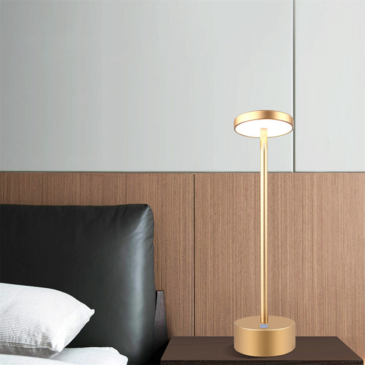 Eine goldfarbene Schreibtischlampe mit rundem Kopf und zylindrischem Sockel, auf einem dunklen Holztisch.