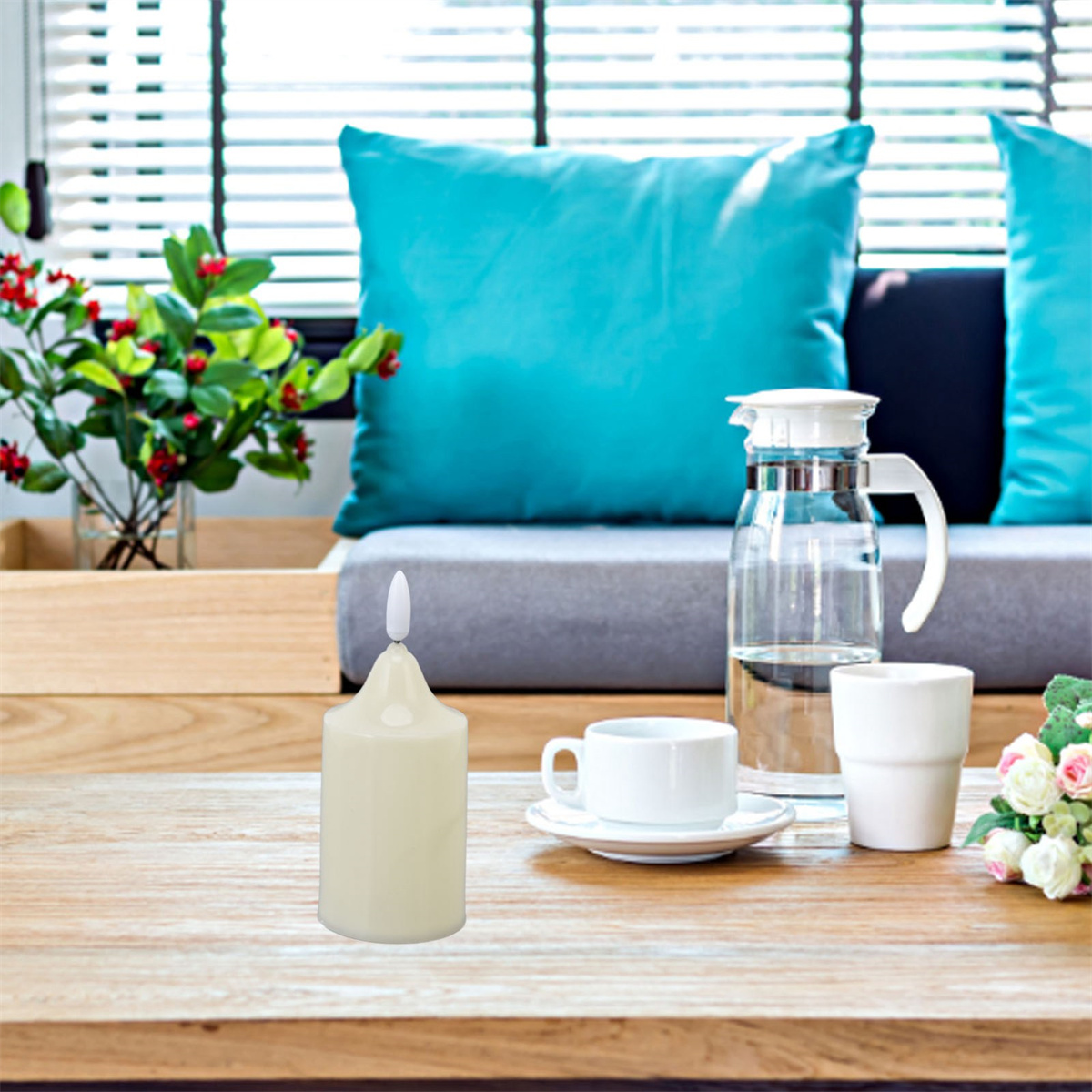 Eine brennende Kerze auf einem Holztisch mit Teetasse, Wasserkrug und Blumen in einer Vase.