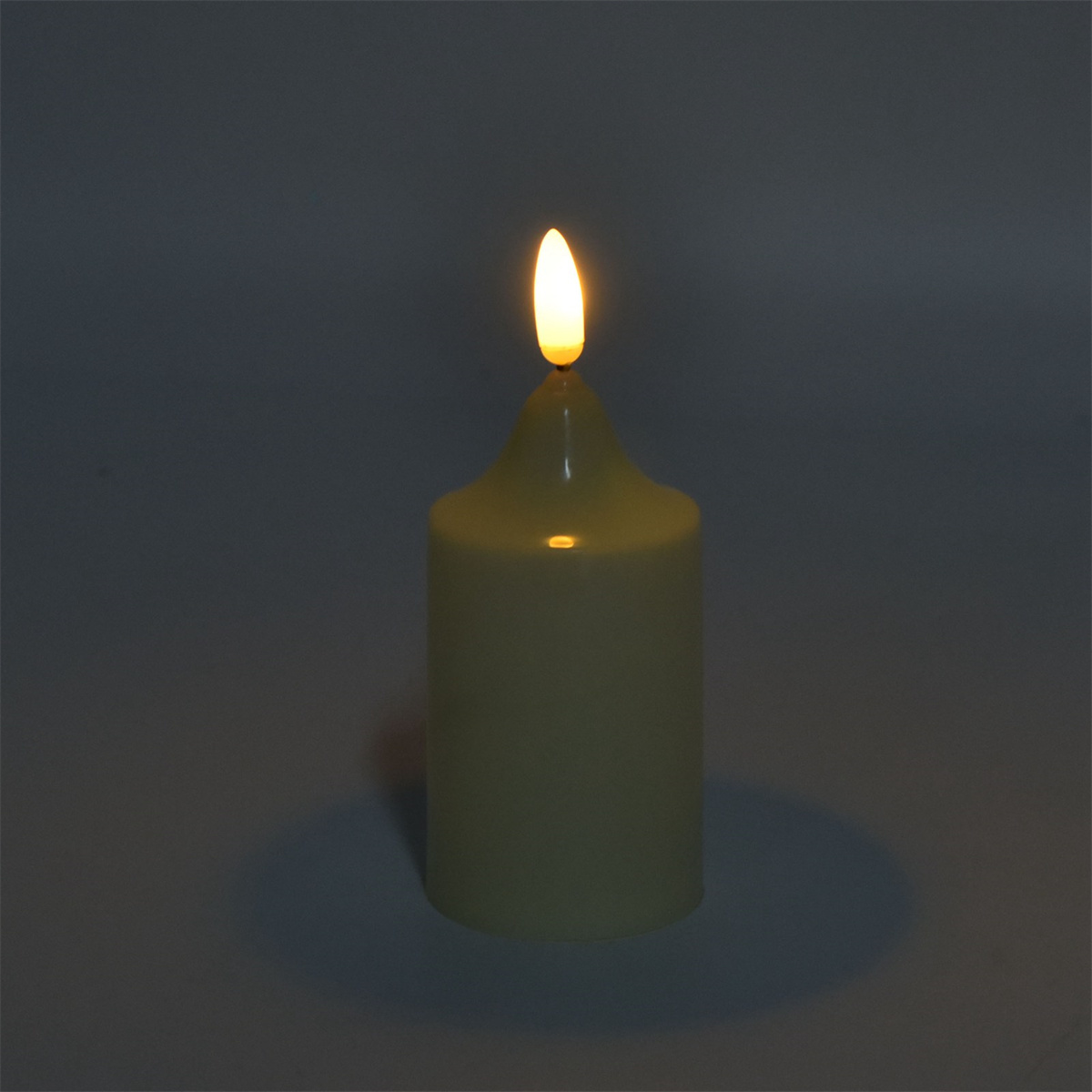 Eine brennende Kerze leuchtet im Dunkeln. Die Kerze ist weiß mit gelber Flamme.