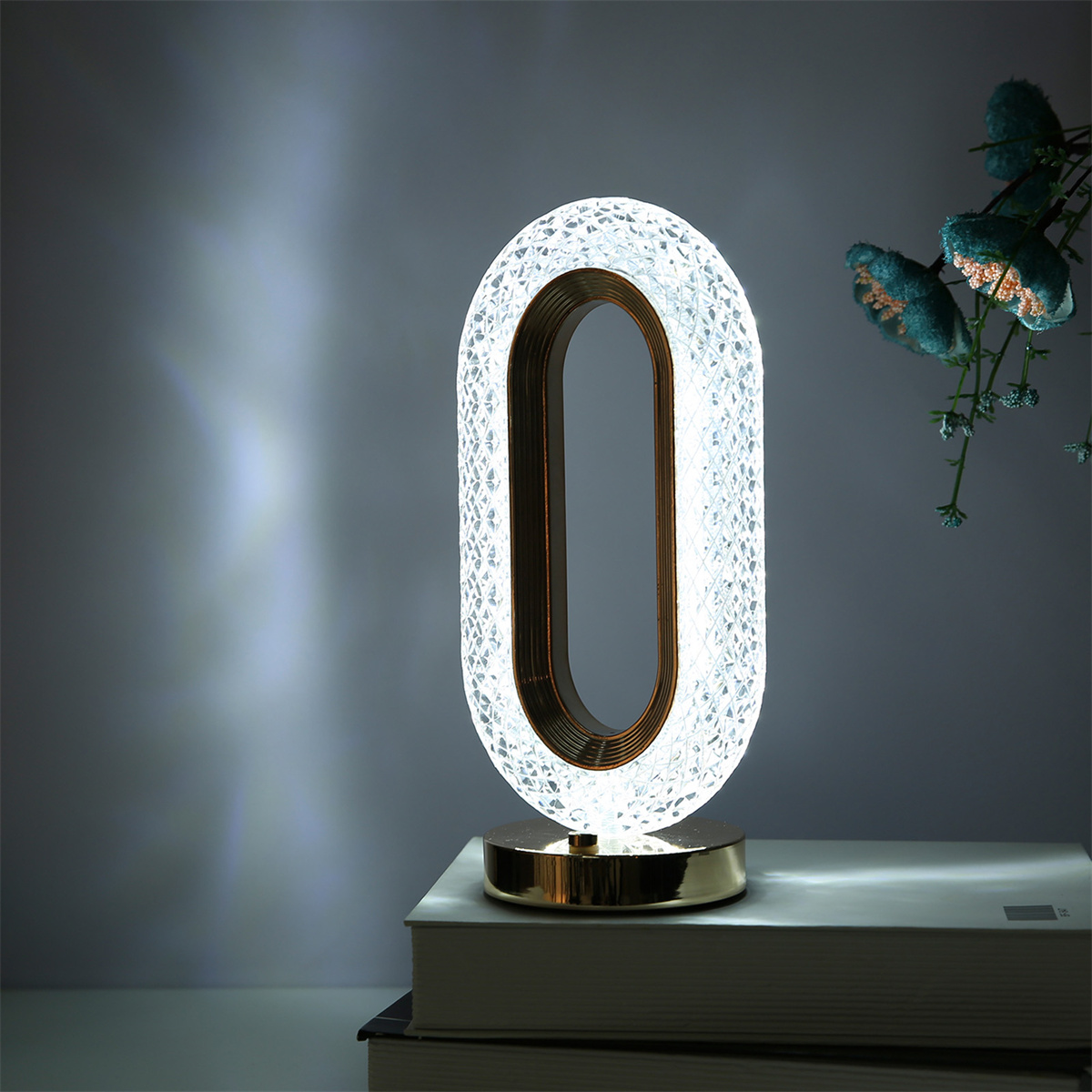 Eine ovale Lampe mit goldenem Sockel und Innenring, hell beleuchtet, auf Büchern.