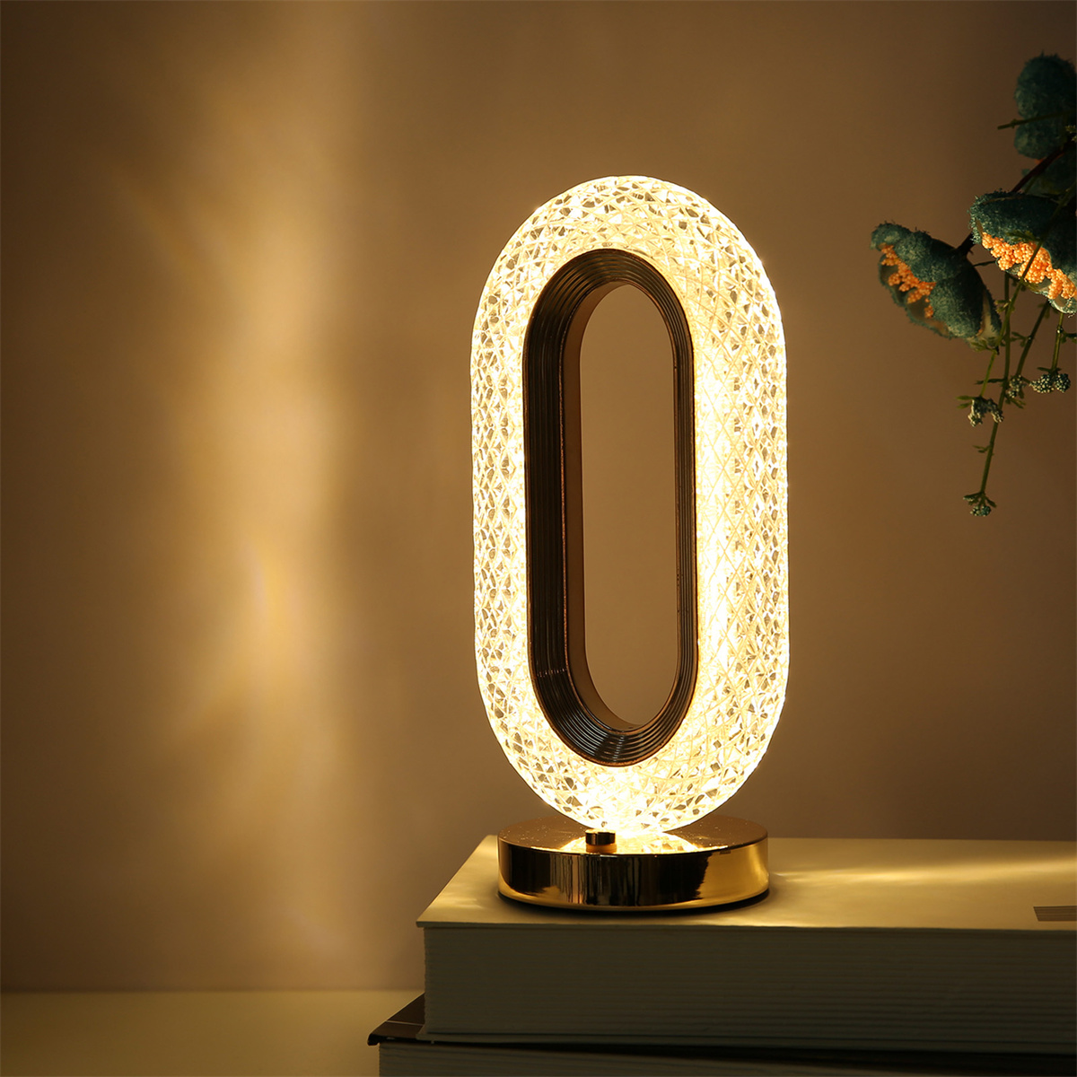 Eine beleuchtete, ovale Tischlampe auf einem Bücherstapel. Sie hat einen goldenen Sockel und einen braunen Rahmen.