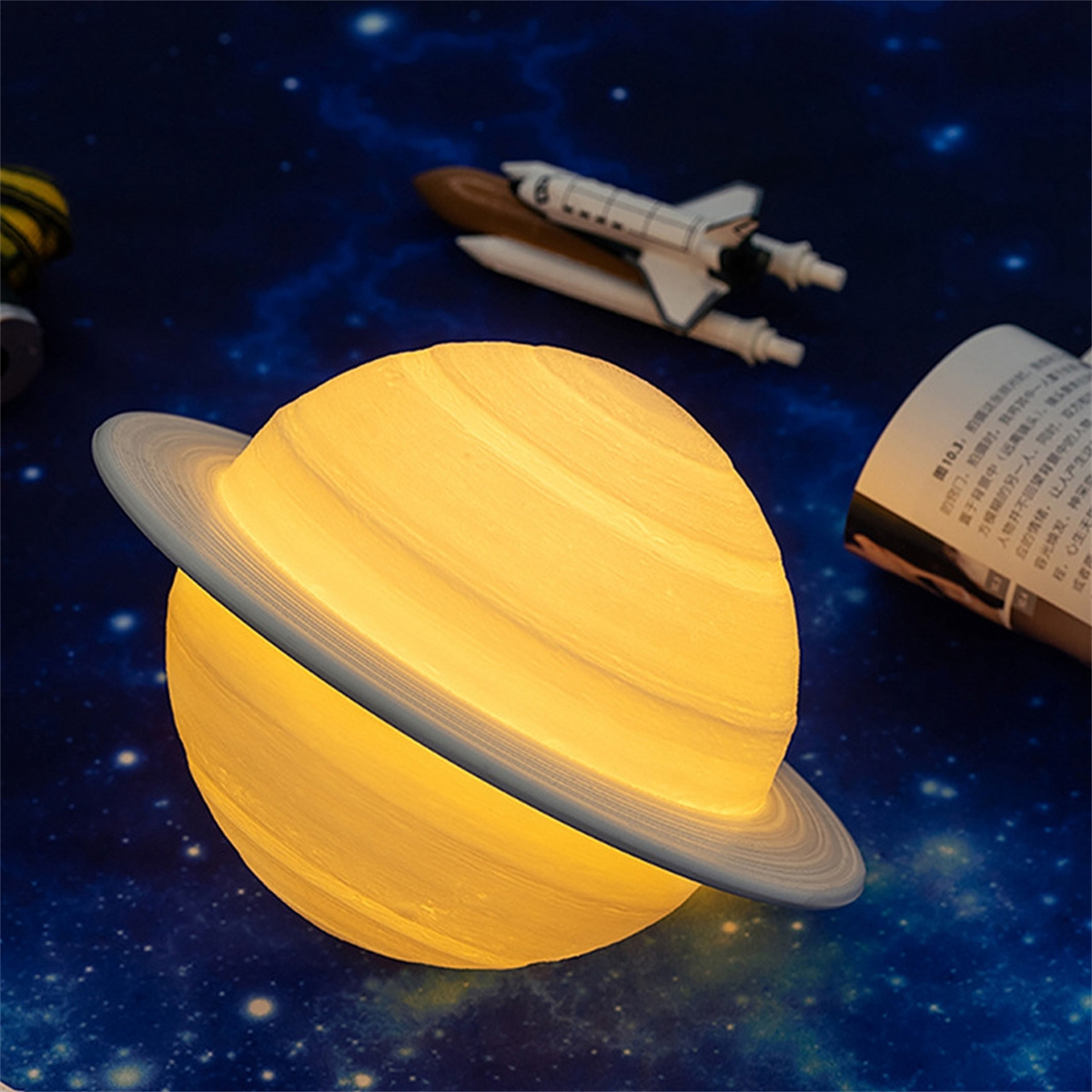 Saturnförmige Lampe, gelb leuchtend. Eine Weltraumszene mit Shuttle und Buch im Hintergrund.