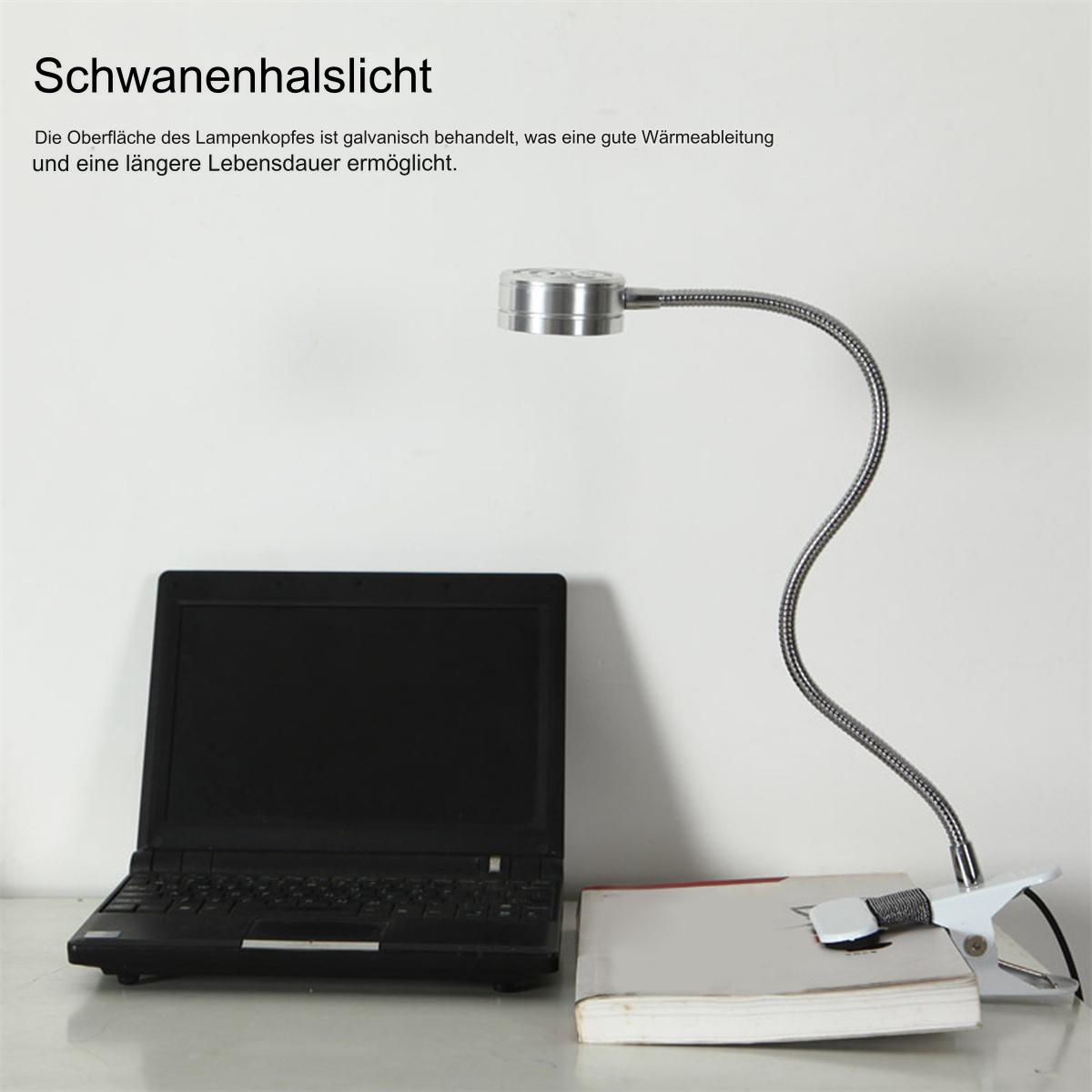 Schwanenhalslampe an einem Buch befestigt, Laptop auf dem Schreibtisch. Text auf Deutsch sichtbar.