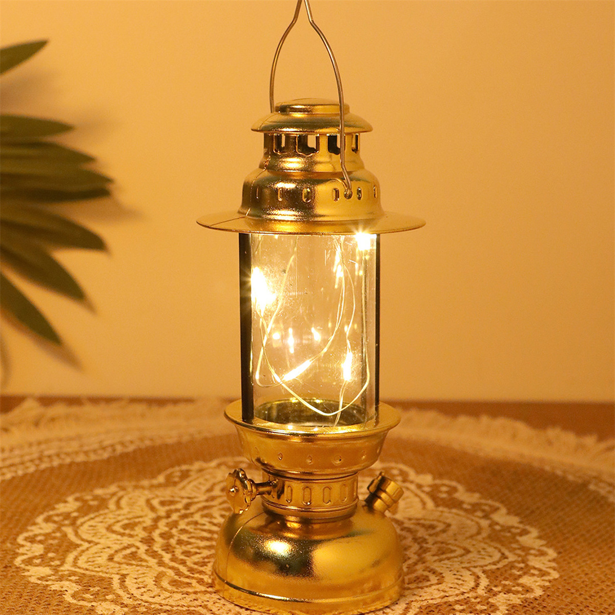 Goldfarbene Laterne mit Glasteil und leuchtenden Lichtern, auf einem Tisch.
