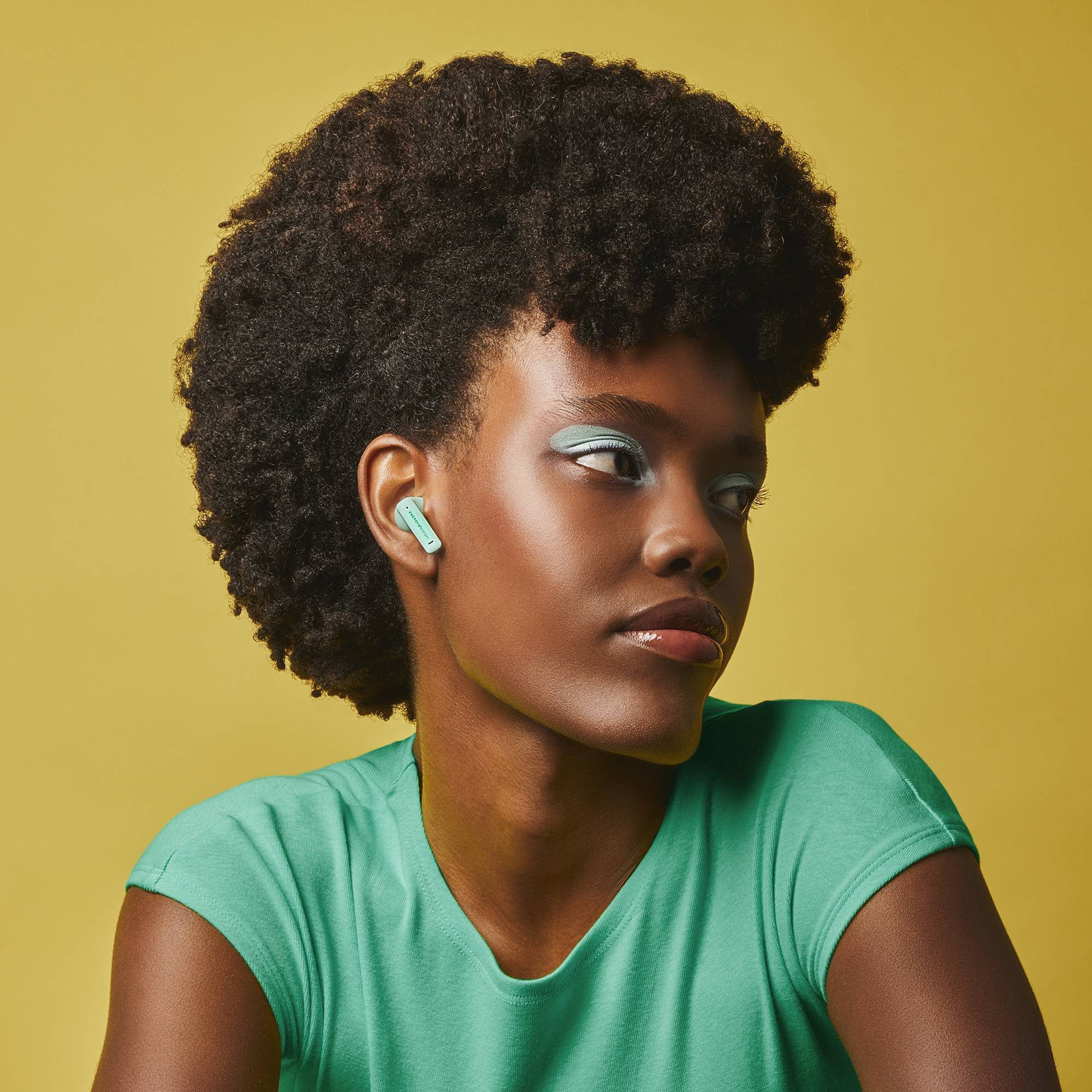 Una donna con auricolari verdi, che guarda a destra, con ombretto verde acqua e una camicia verde.