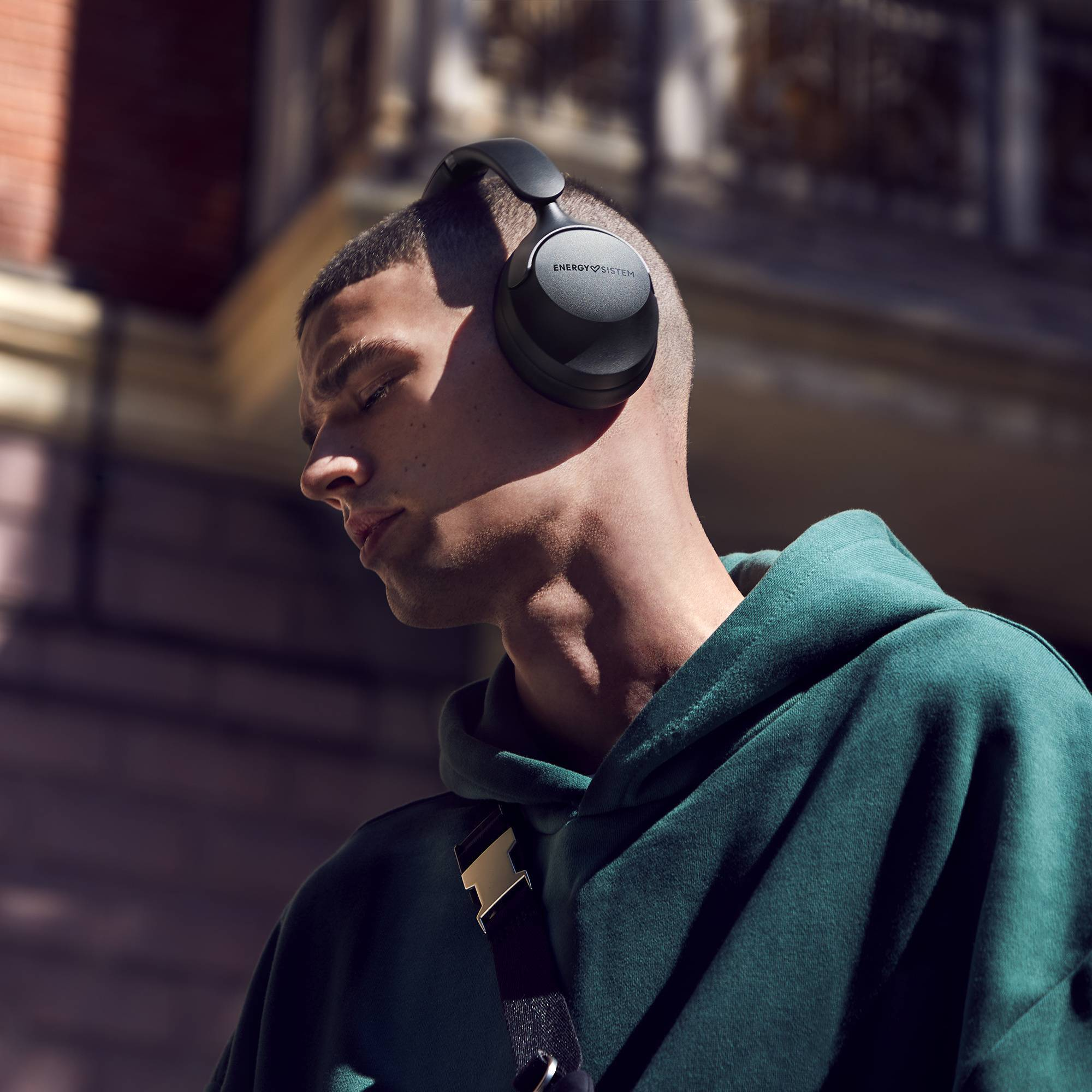 Un uomo con cuffie nere e felpa con cappuccio verde in un ambiente urbano.