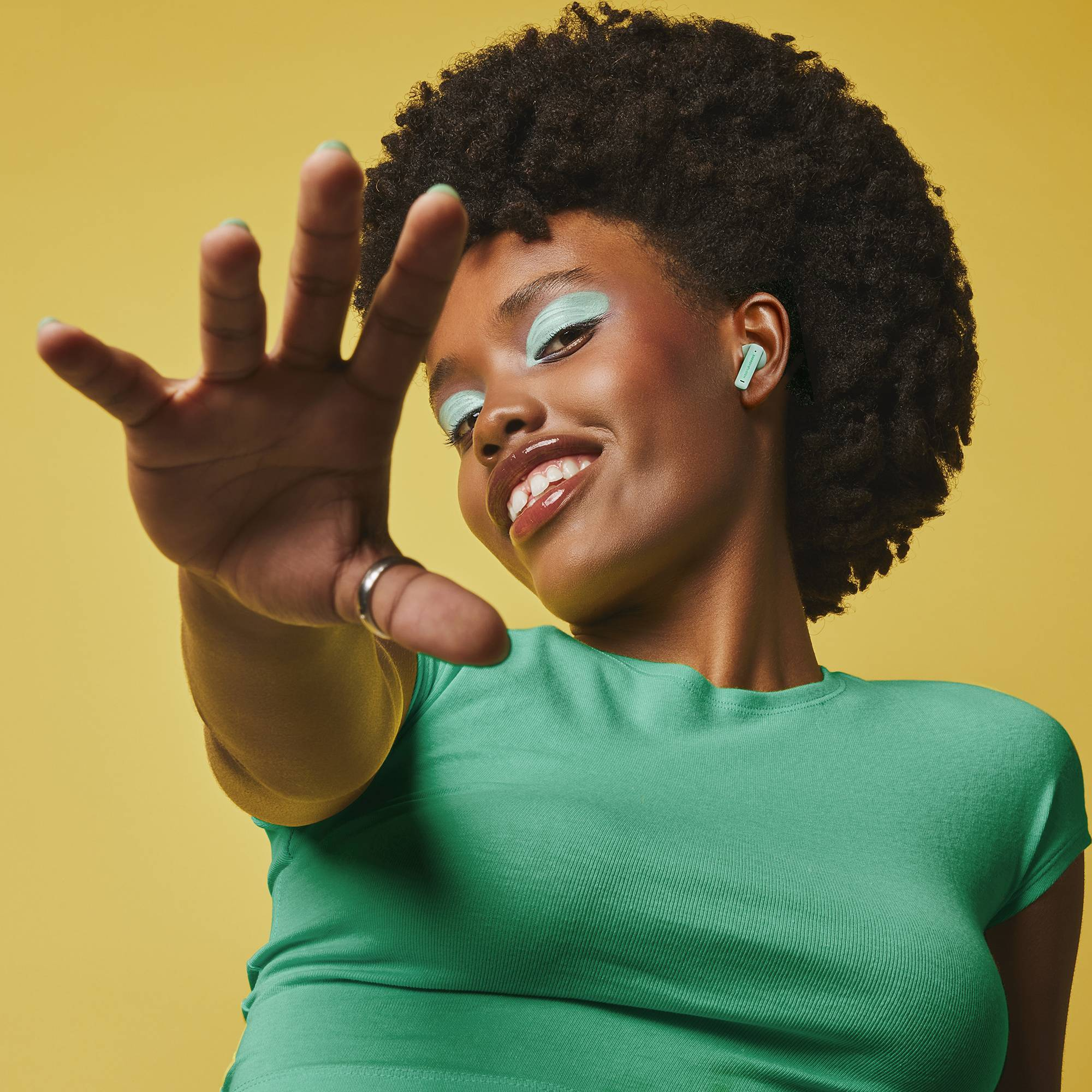 Donna sorridente con afro e ombretto verde menta che stende la mano. Indossa auricolari verde menta.