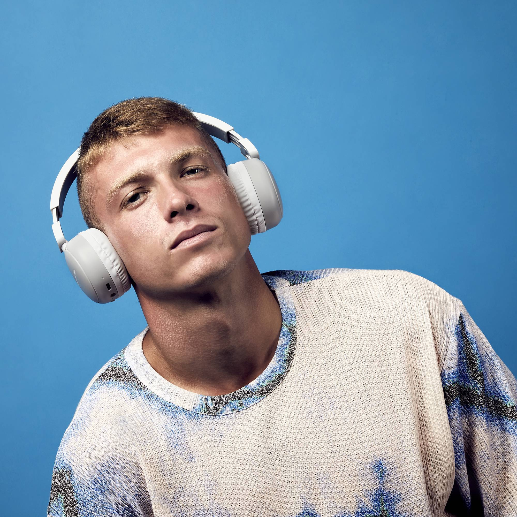 Un hombre con auriculares sobre un fondo azul. Está mirando al espectador.
