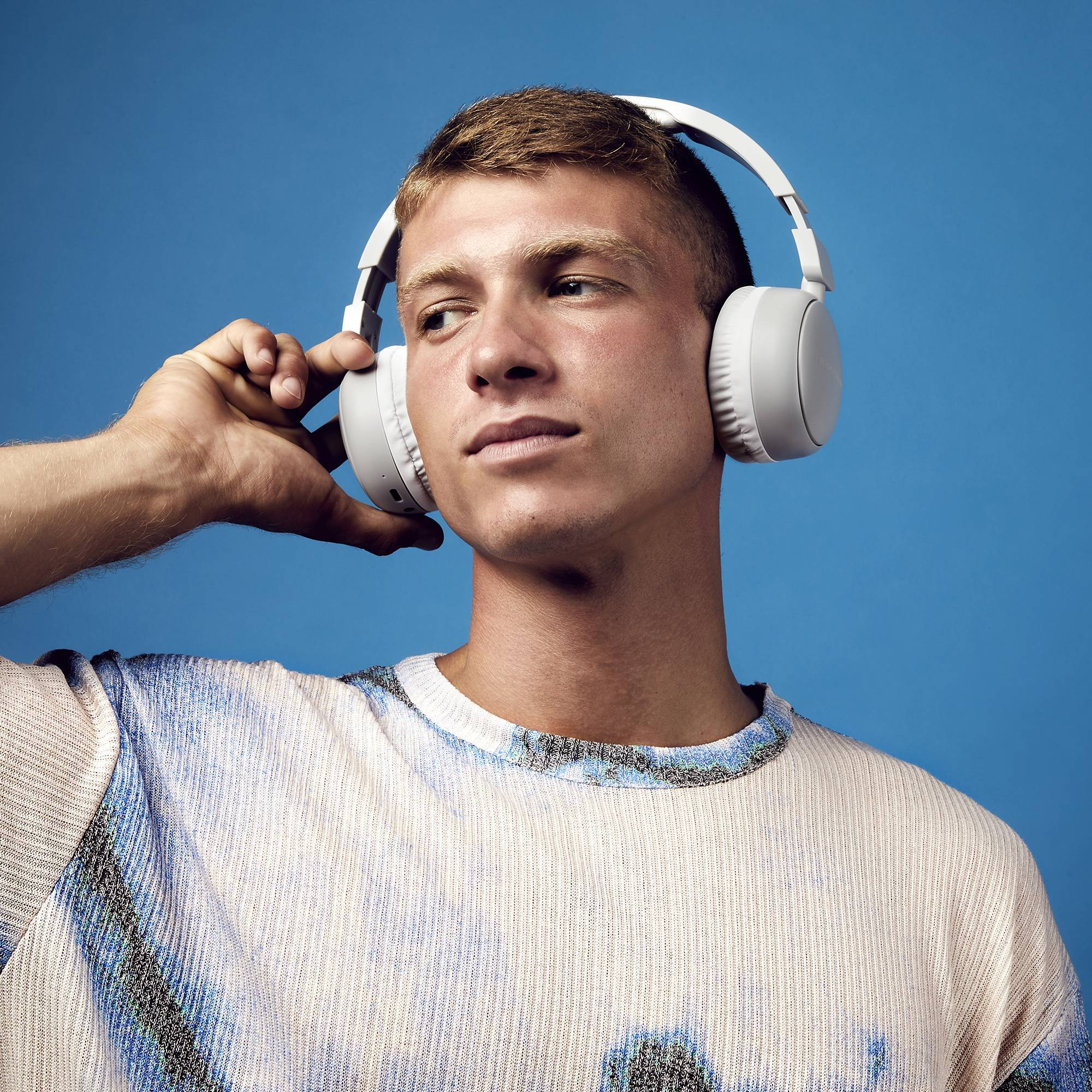 Joven con auriculares blancos sobre la oreja sobre un fondo azul.