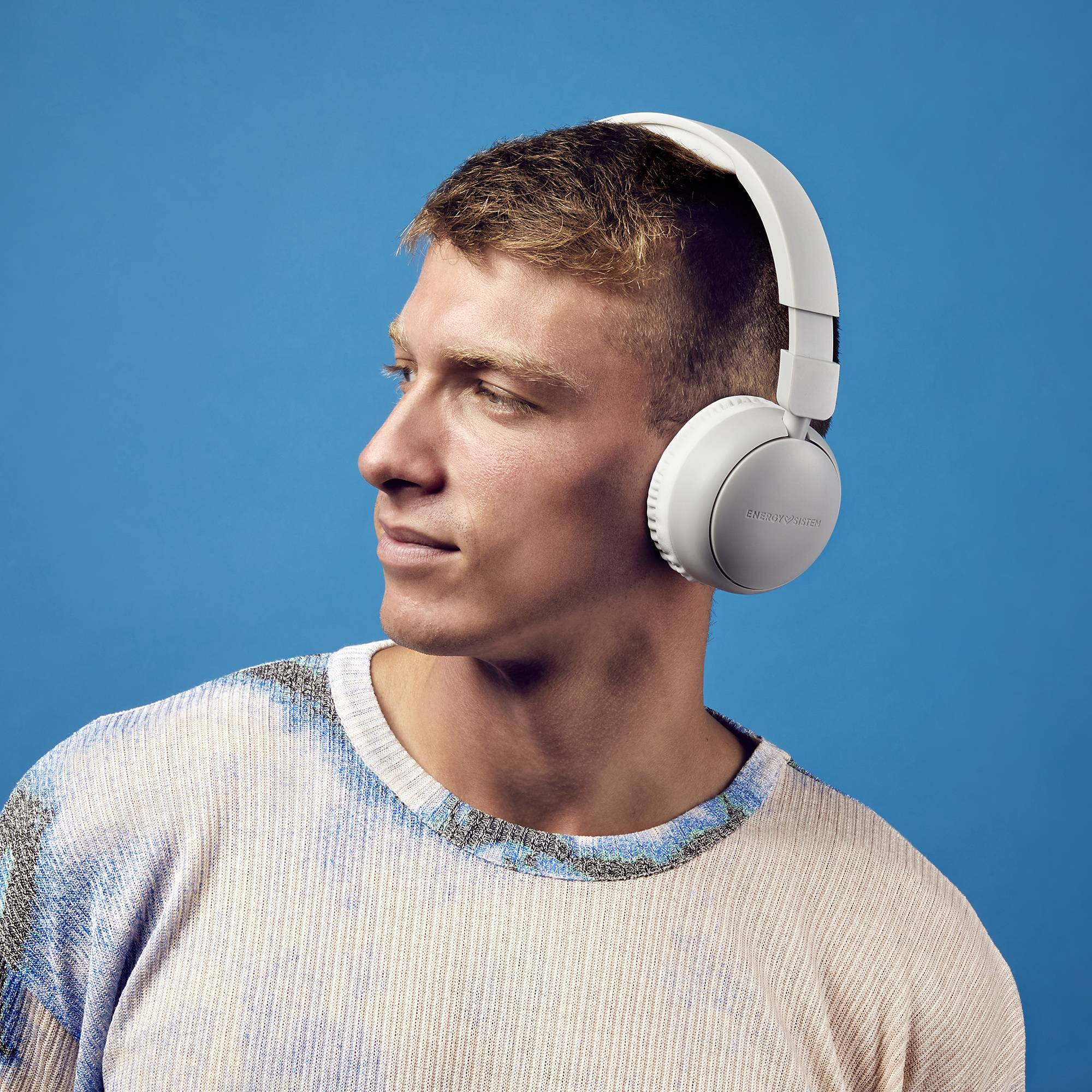 Un hombre con auriculares blancos, mirando hacia un lado, con fondo azul.