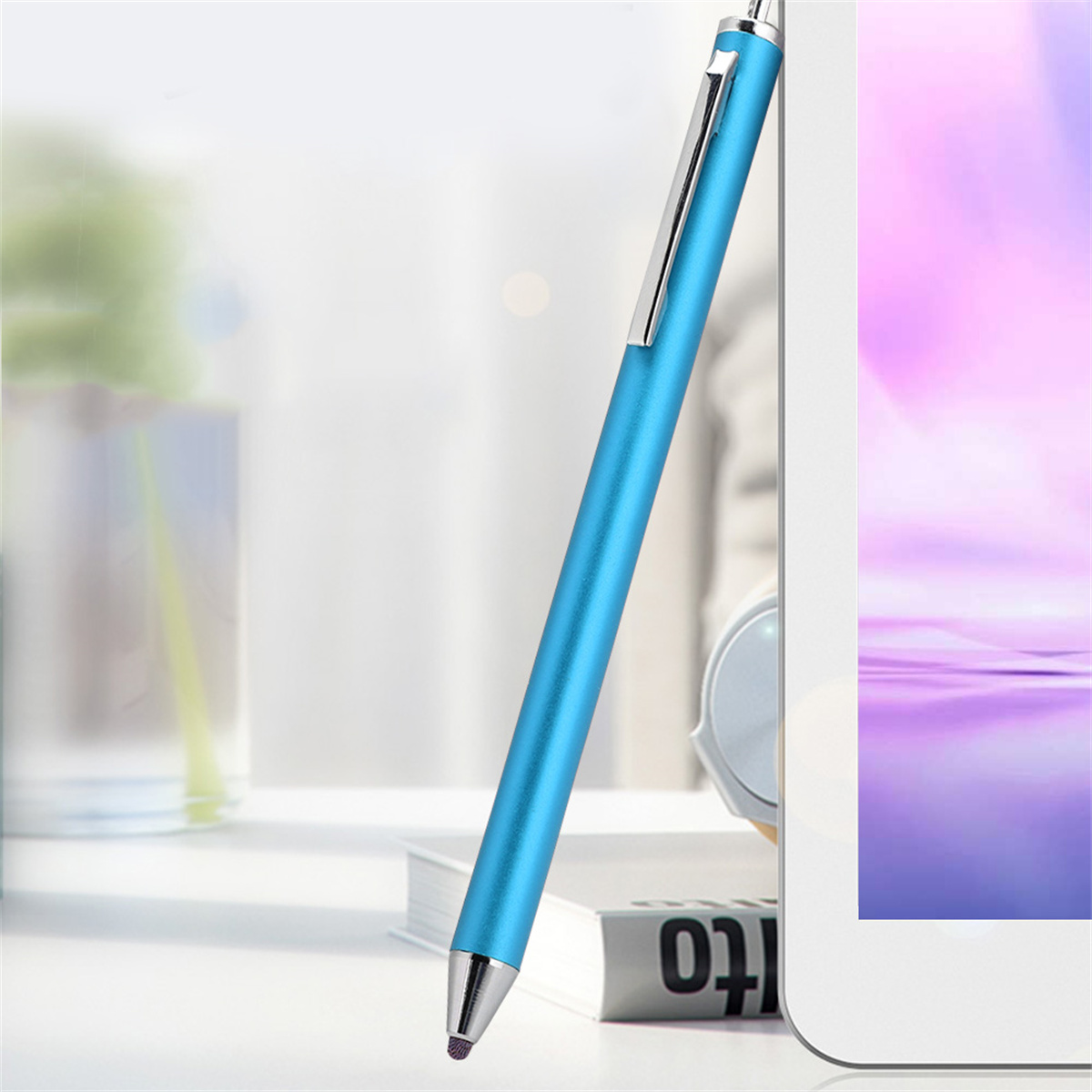 Ein hellblauer Stylus-Stift, der sich an ein Tablet lehnt, auf einer weißen Oberfläche mit einem Buch.