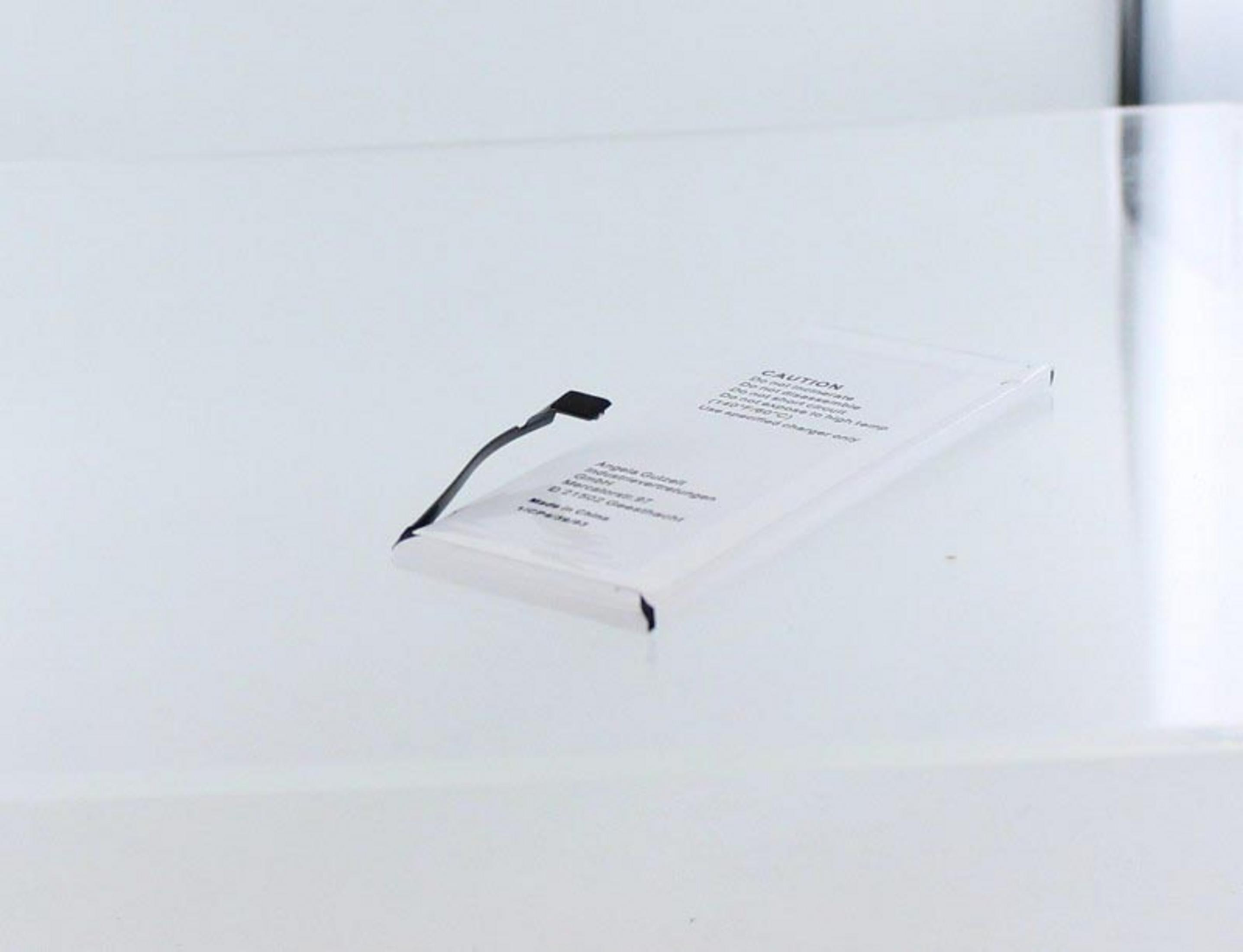Ein weißes rechteckiges Batteriepack auf einer klaren Oberfläche. Vorsichtshinweis ist auf der Batterieoberfläche sichtbar.