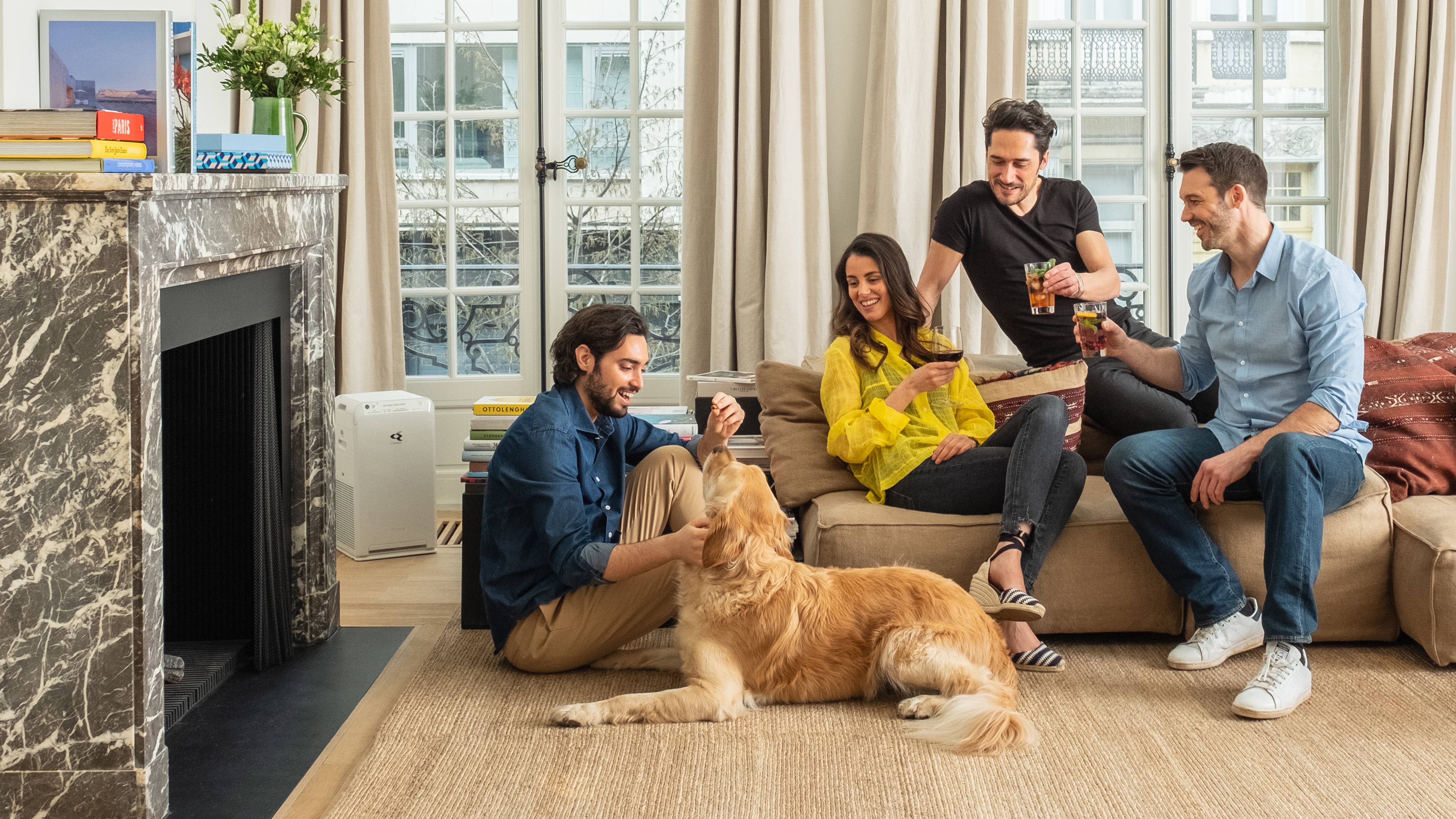 Quatre personnes et un chien dans un salon. Deux hommes et une femme sont assis et debout.