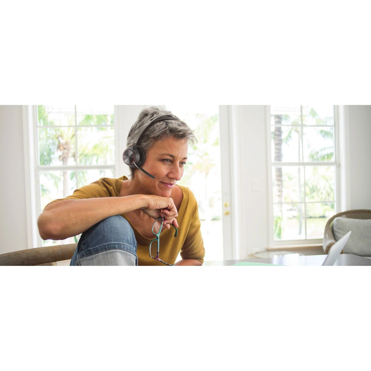 Donna con cuffie, seduta vicino a un laptop e una finestra.