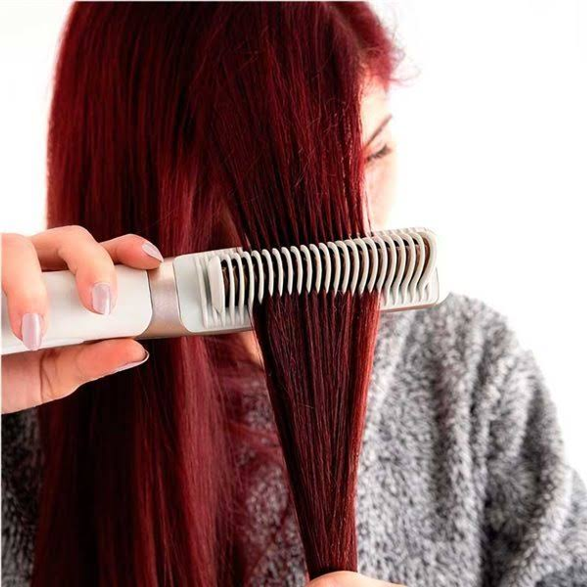Persona che si pettina i capelli rossi con una piastra. I capelli sono lunghi e rosso scuro.