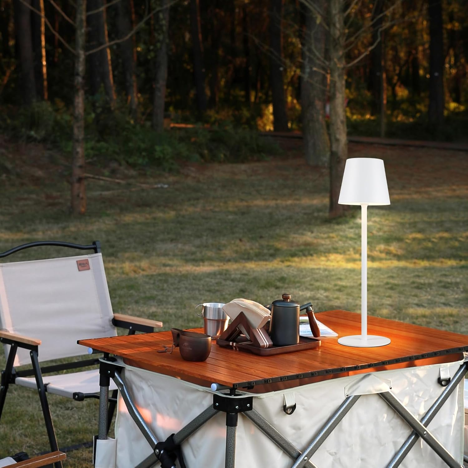 Scena all'aperto: un tavolo illuminato con lampada, cibo, bevande e foresta sullo sfondo.