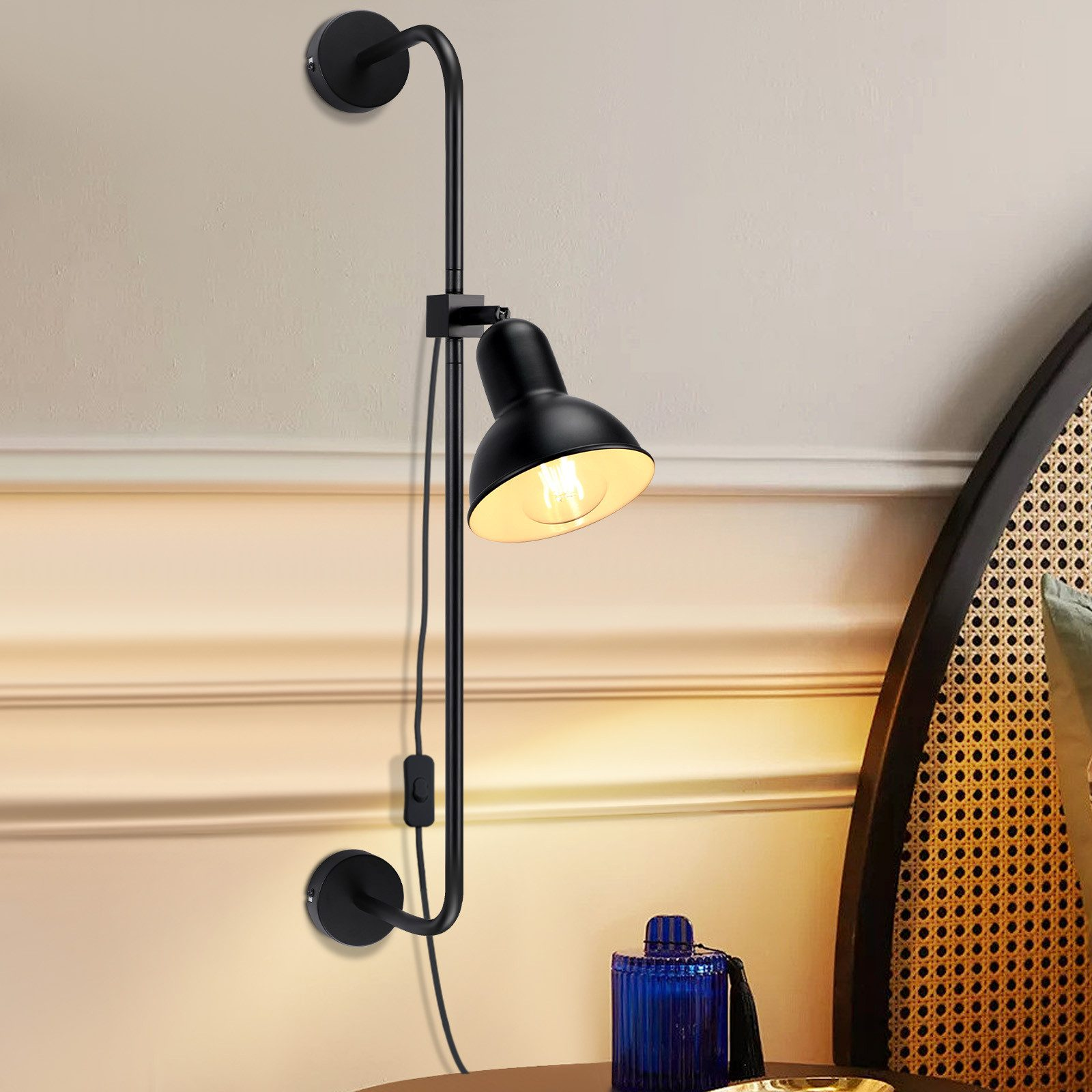 Czarna lampa ścienna na beżowej ścianie z niebieskim szklanym wazonem. Z przełącznikiem i przewodem.