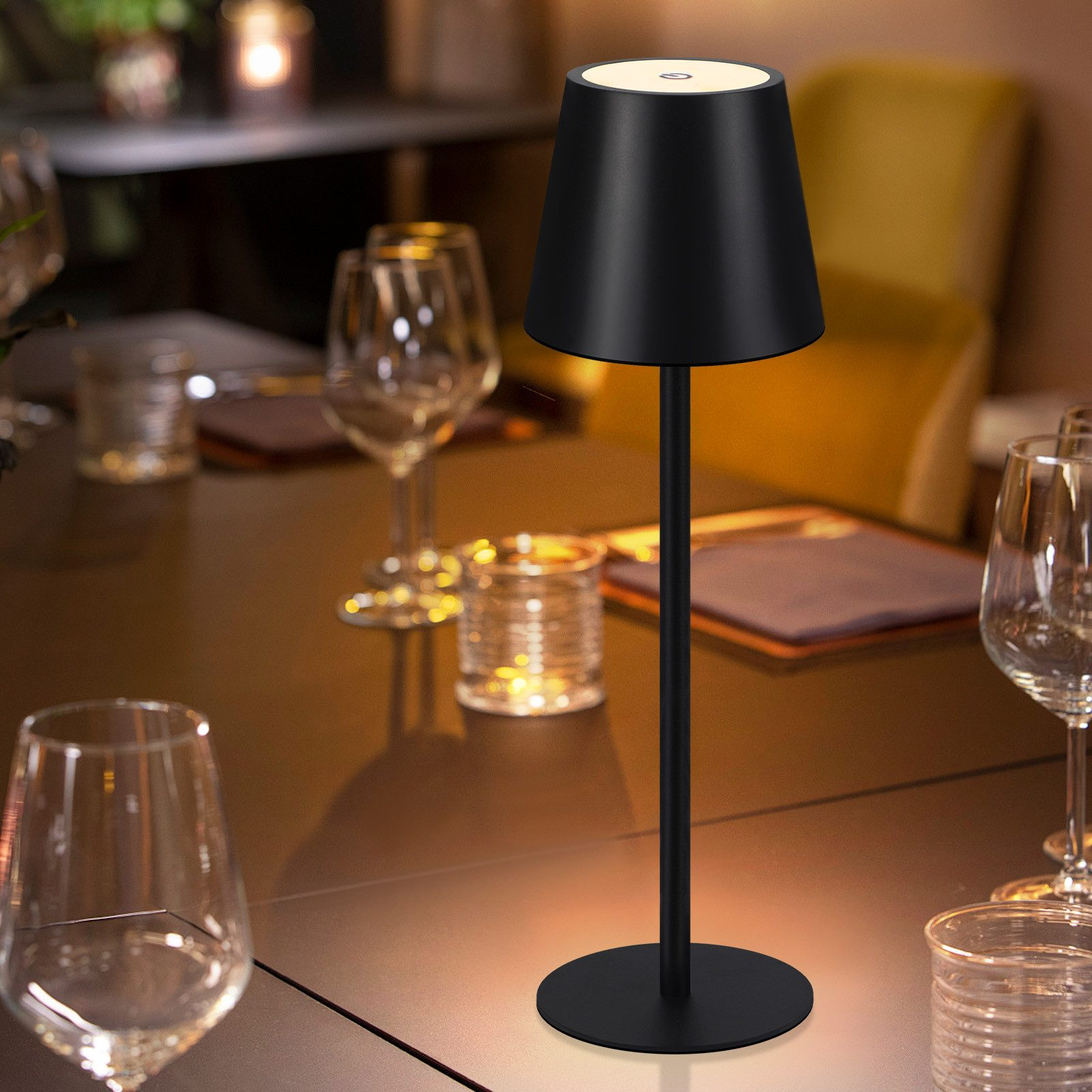 Lampada da tavolo nera su un tavolo, illuminata, con bicchieri e acqua.