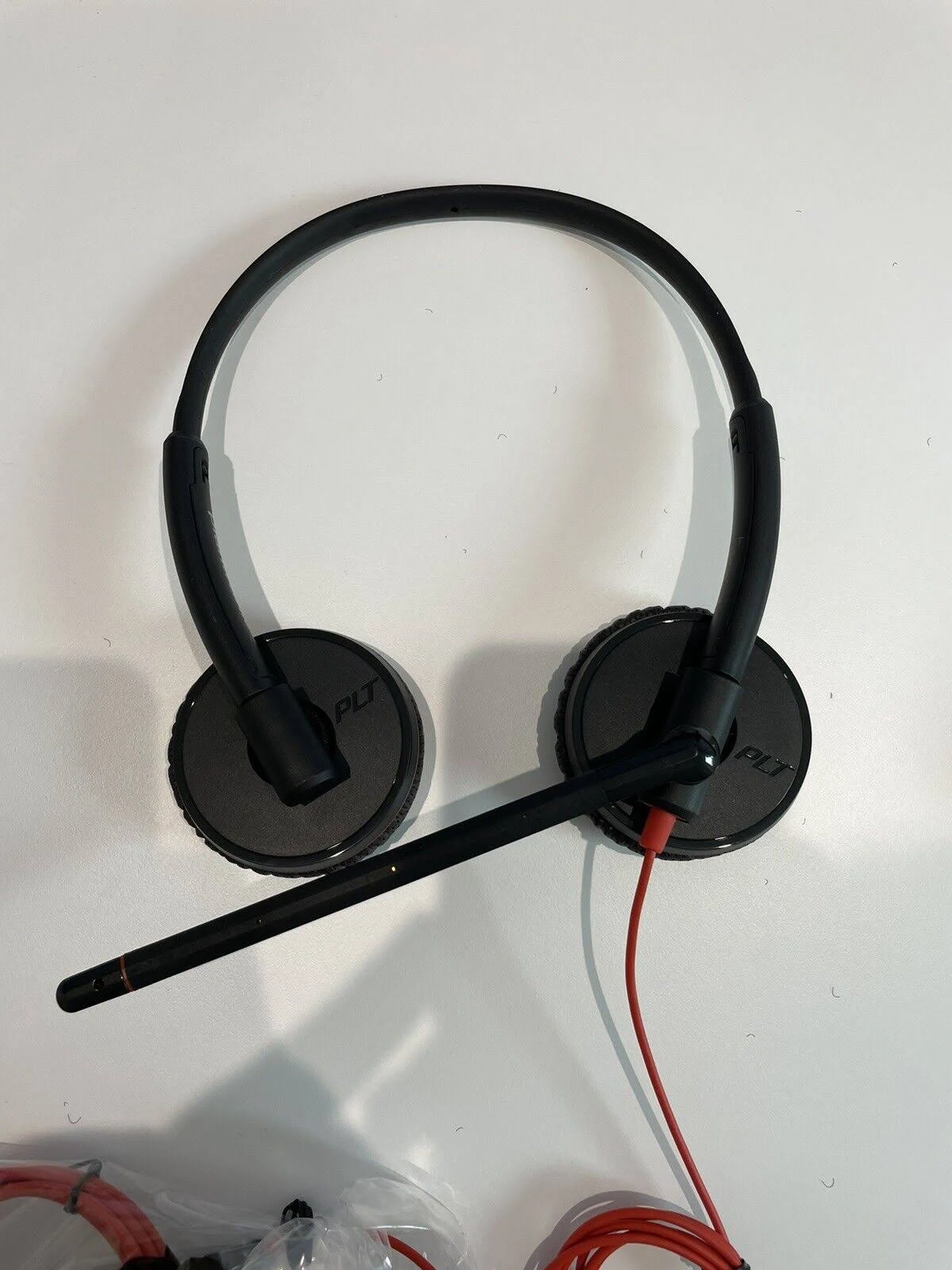 Headset met zwarte oorschelpen en een rode kabel, op een wit oppervlak.