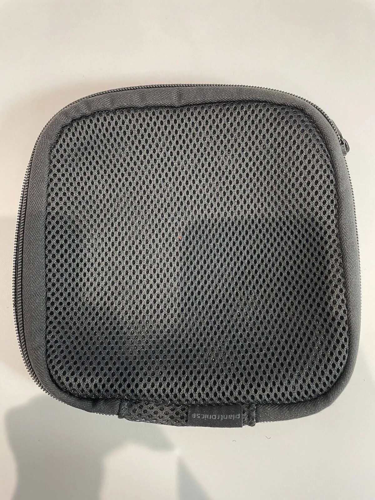 Close-up van een grijze mesh etui met ritssluiting. De merknaam Plantronics is zichtbaar.