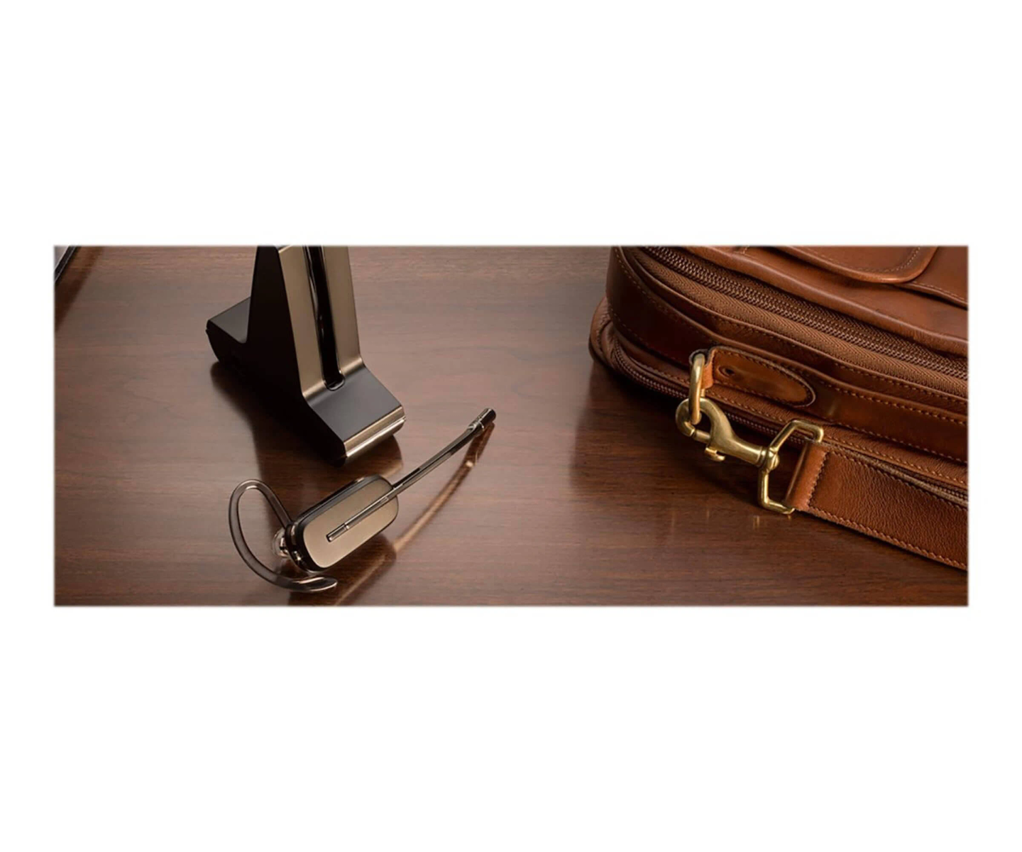 Un auricolare nero è su una scrivania di legno accanto a una borsa di cuoio marrone.