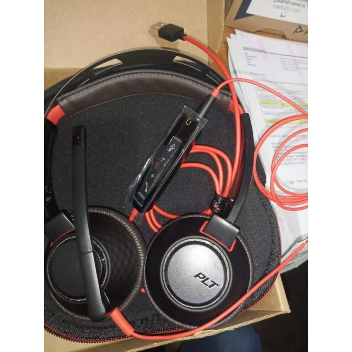 Casque noir avec câbles rouges et microphone. Placé à l'intérieur d'un étui noir.