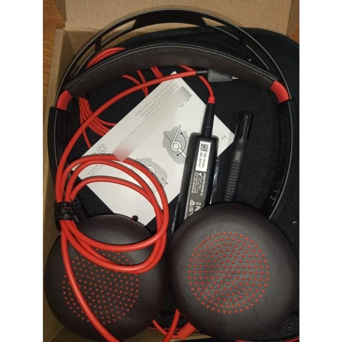 Casque rouge et noir avec câbles rouges, dans une boîte marron avec une feuille d'instructions blanche.