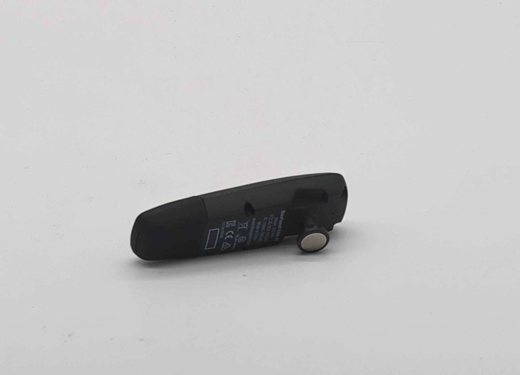Un piccolo dispositivo Bluetooth nero, appoggiato su una superficie bianca. Il dispositivo ha del testo.