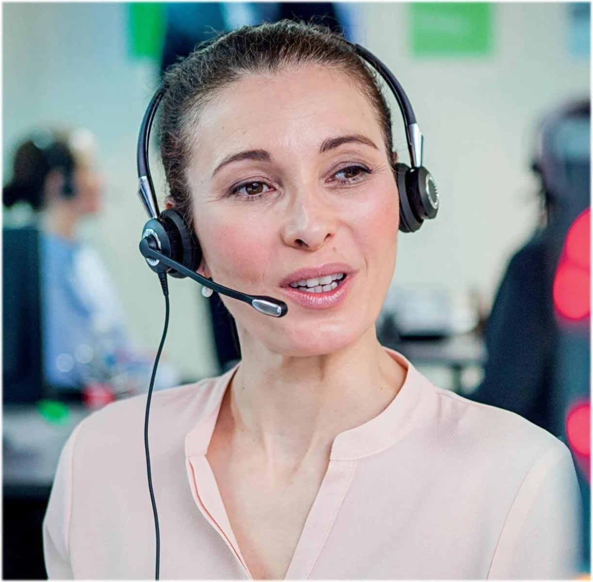 Una donna con cuffie e microfono, sorridente. Sfondo sfocato dell'ufficio.