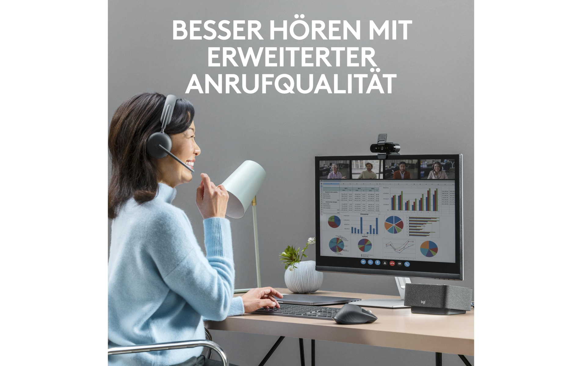 Kobieta w zestawie słuchawkowym, używająca komputera z kamerą internetową i dwoma głośnikami na biurku, szare tło.