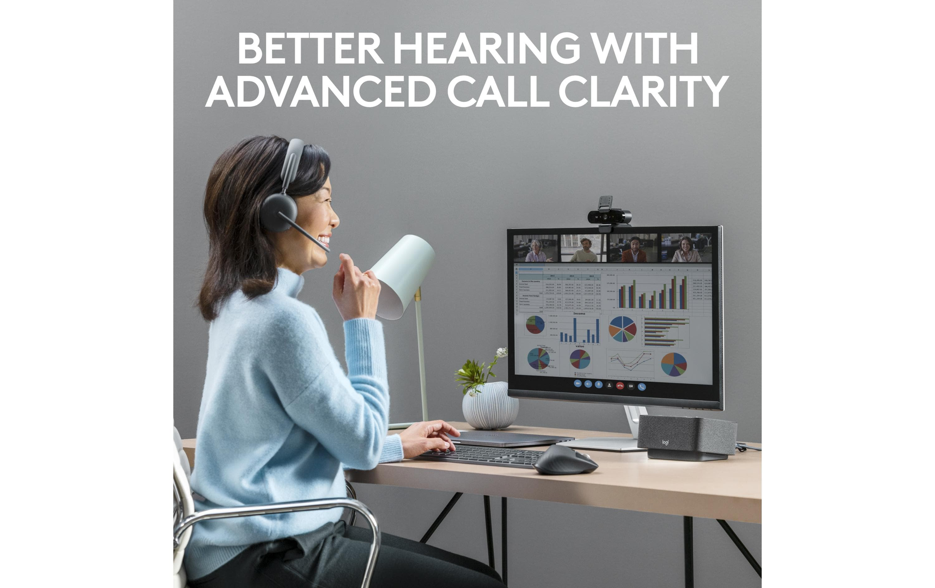 Kobieta z zestawem słuchawkowym w trakcie rozmowy, ekran pokazuje połączenia wideo i wykresy, lampa i klawiatura z przodu.