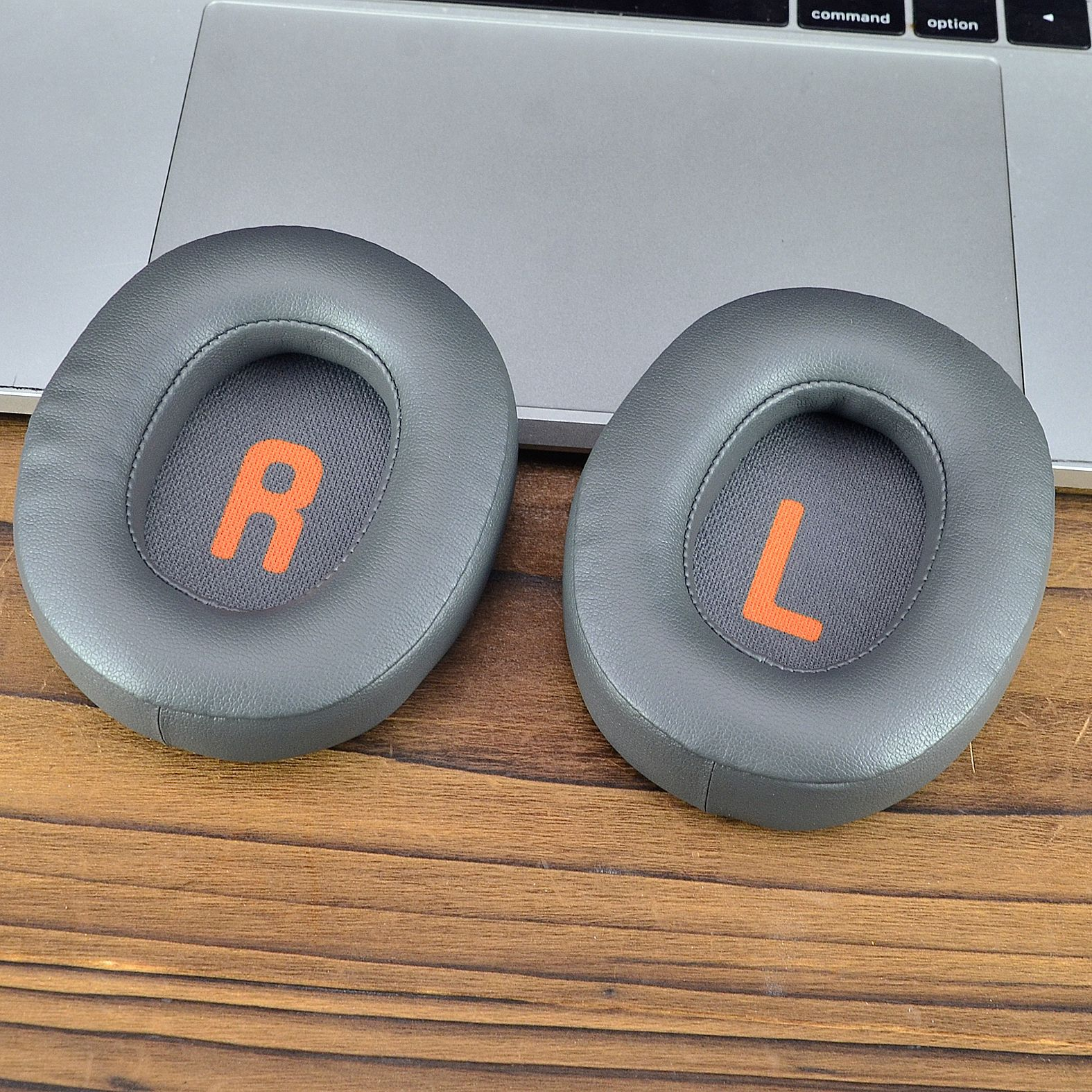 Zwei graue Kopfhörer-Ohrpolster mit orangefarbenem 'R' und 'L' auf einer Laptop-Tastatur.