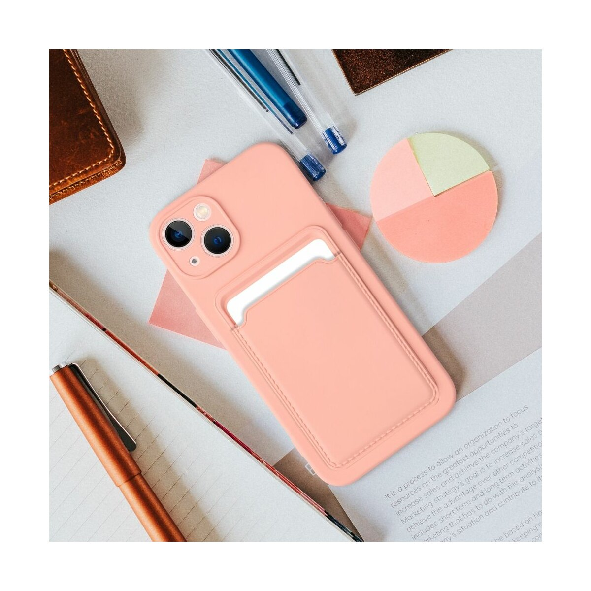 Custodia rosa per telefono con porta carte, su una scrivania. Altri oggetti presenti.