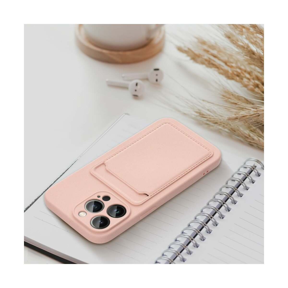 Custodia rosa per telefono con porta carte su tavolo bianco con auricolari e taccuino.