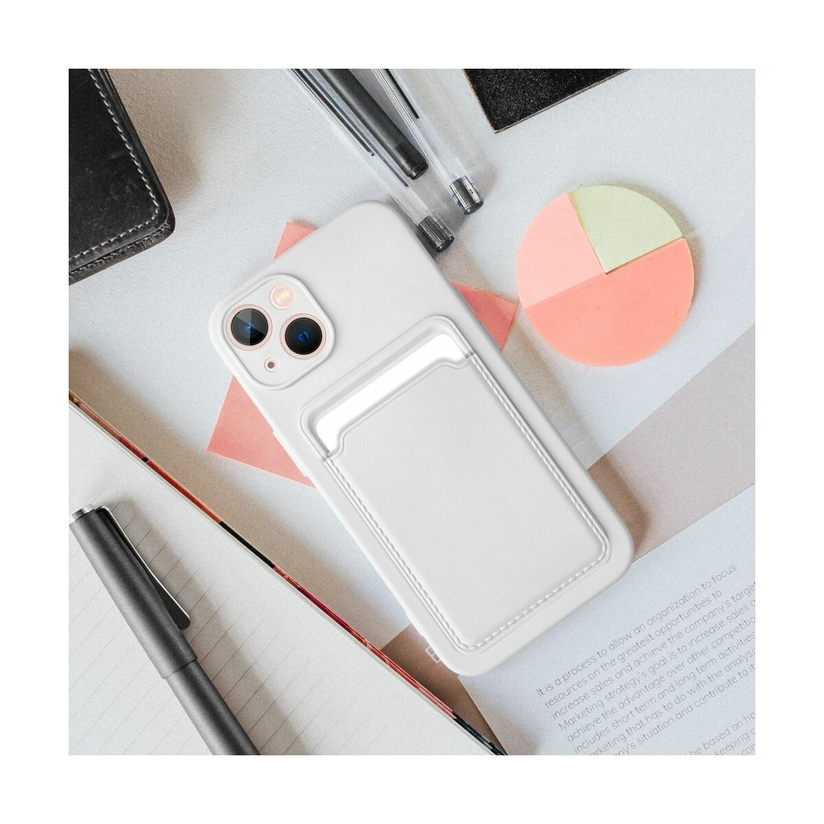 iPhone bianco con portacarte bianco su una scrivania con penne e un appunto rosa.