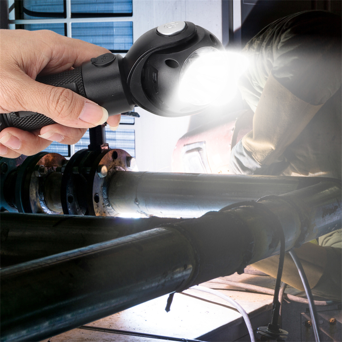 Eine Taschenlampe, die von einer Hand gehalten wird, beleuchtet Metallrohre. Person im Hintergrund, Schweißen.