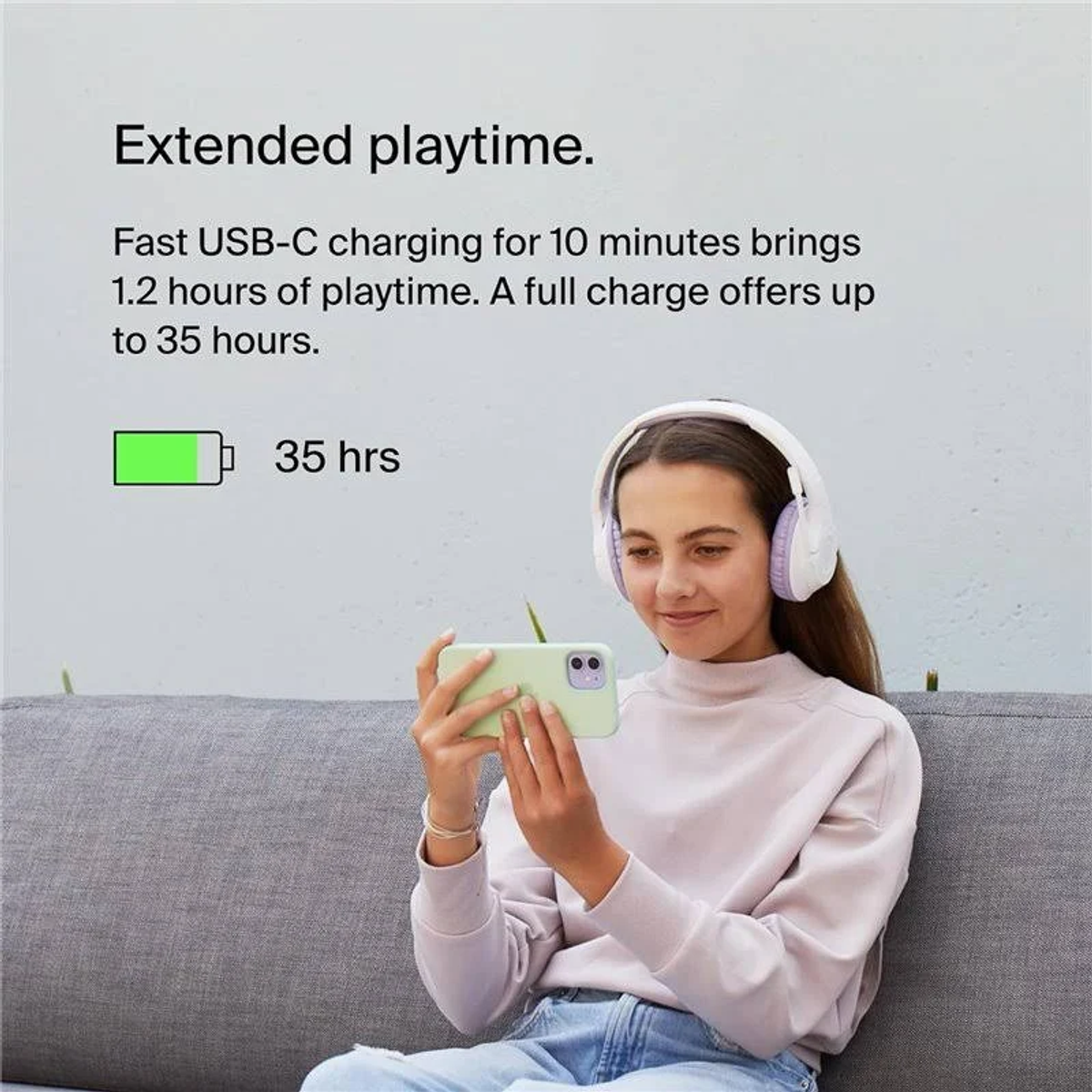 Dziewczyna w różowym swetrze używa telefonu w białych słuchawkach. Ikona baterii pokazuje 35 godzin.