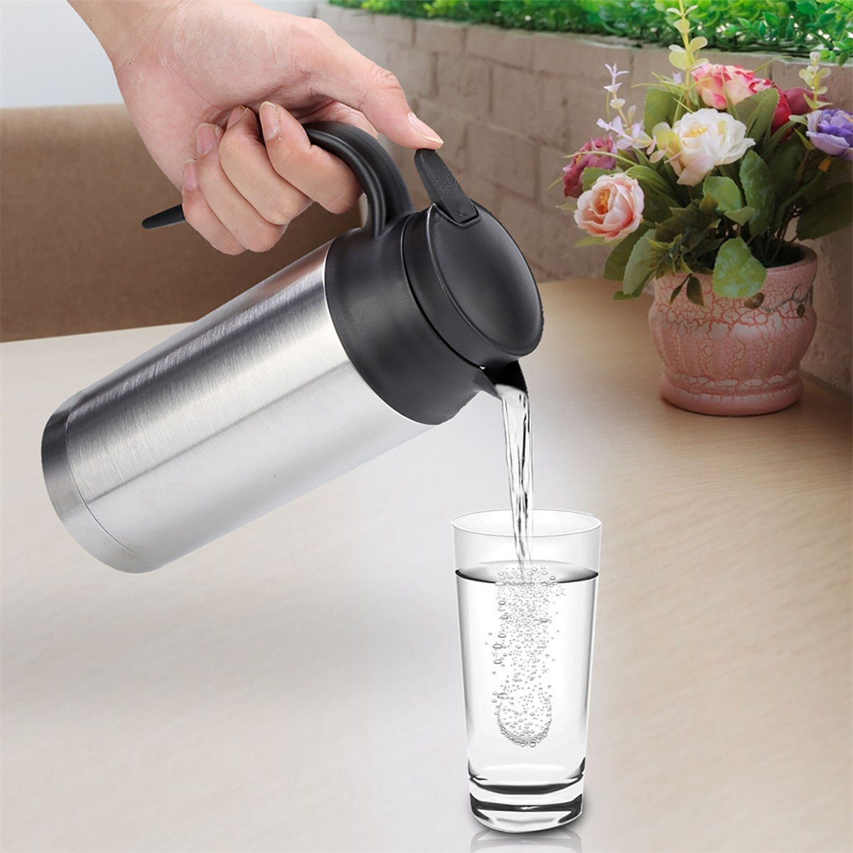 Eine Person gießt Wasser aus einer silbernen Thermoskanne in ein Glas, Blasen sichtbar.