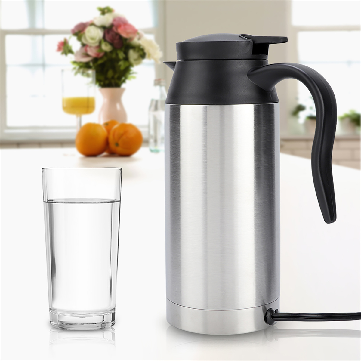 Ein Glas Wasser und ein elektrischer Metallkessel. Eine Vase mit Blumen im Hintergrund.