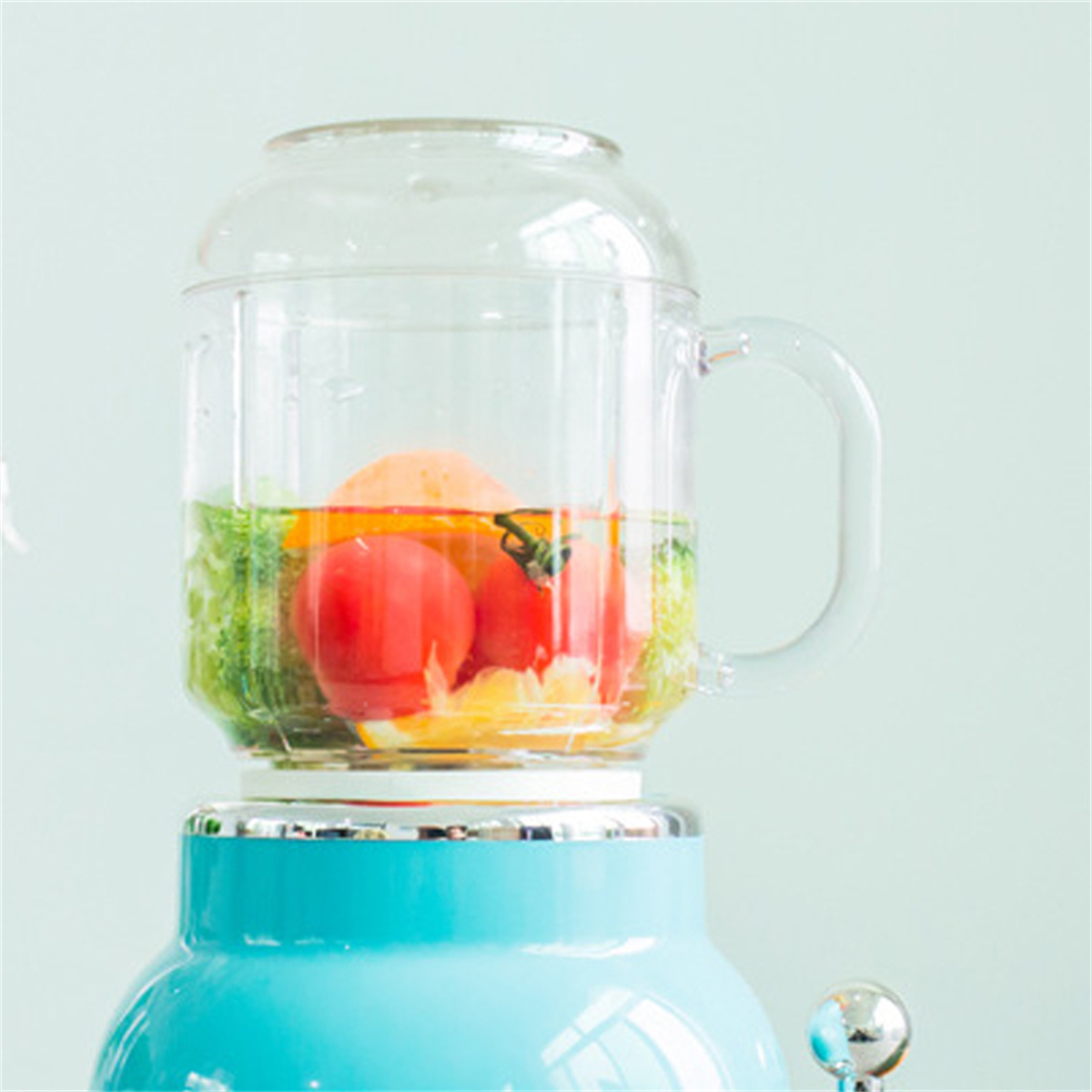 Mixer mit Tomaten, Orangen und Brokkoli im Inneren. Es steht auf einem blauen Sockel, einem klaren Glas.