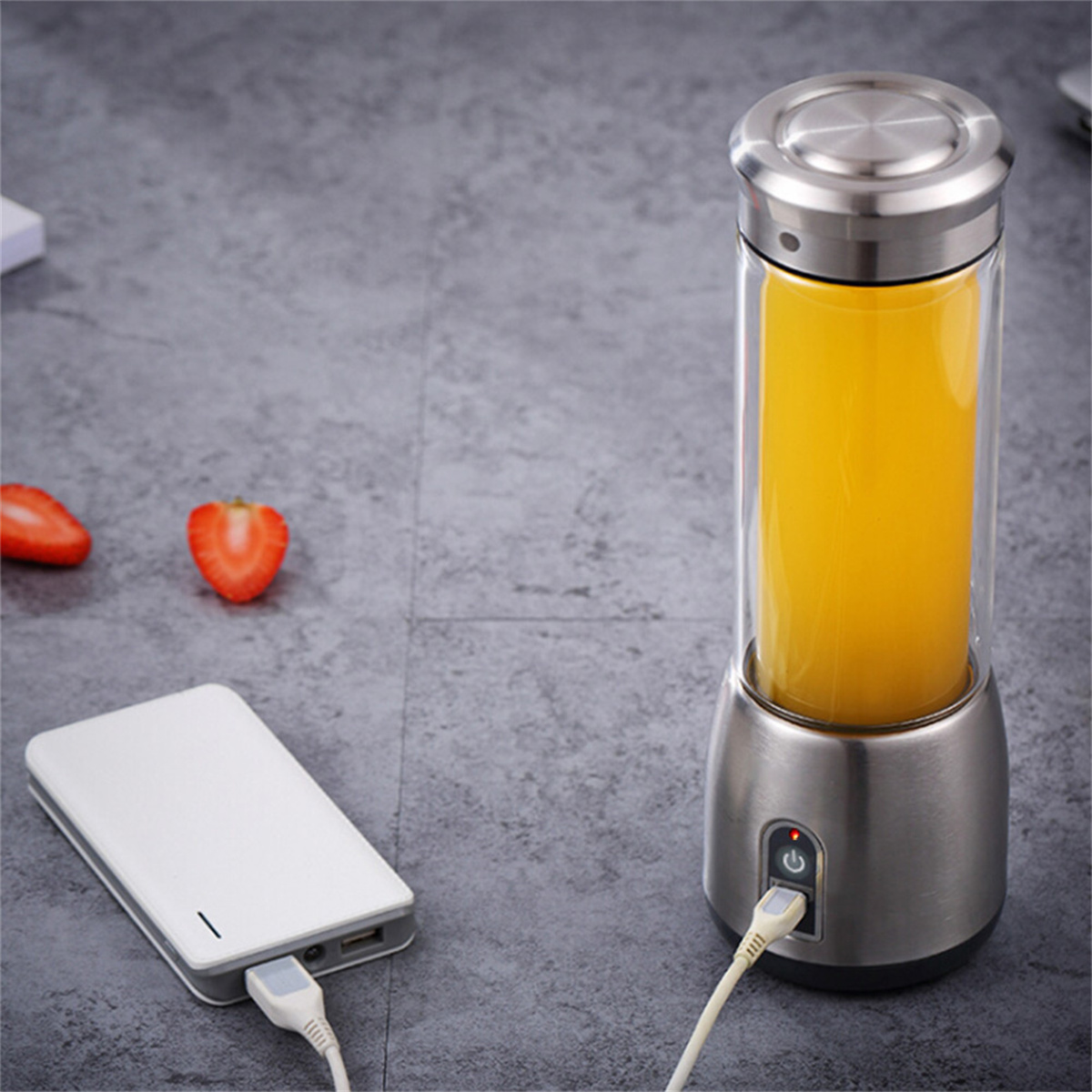 Ein tragbarer Entsafter mit Orangensaft, eine weiße Powerbank und Erdbeeren.