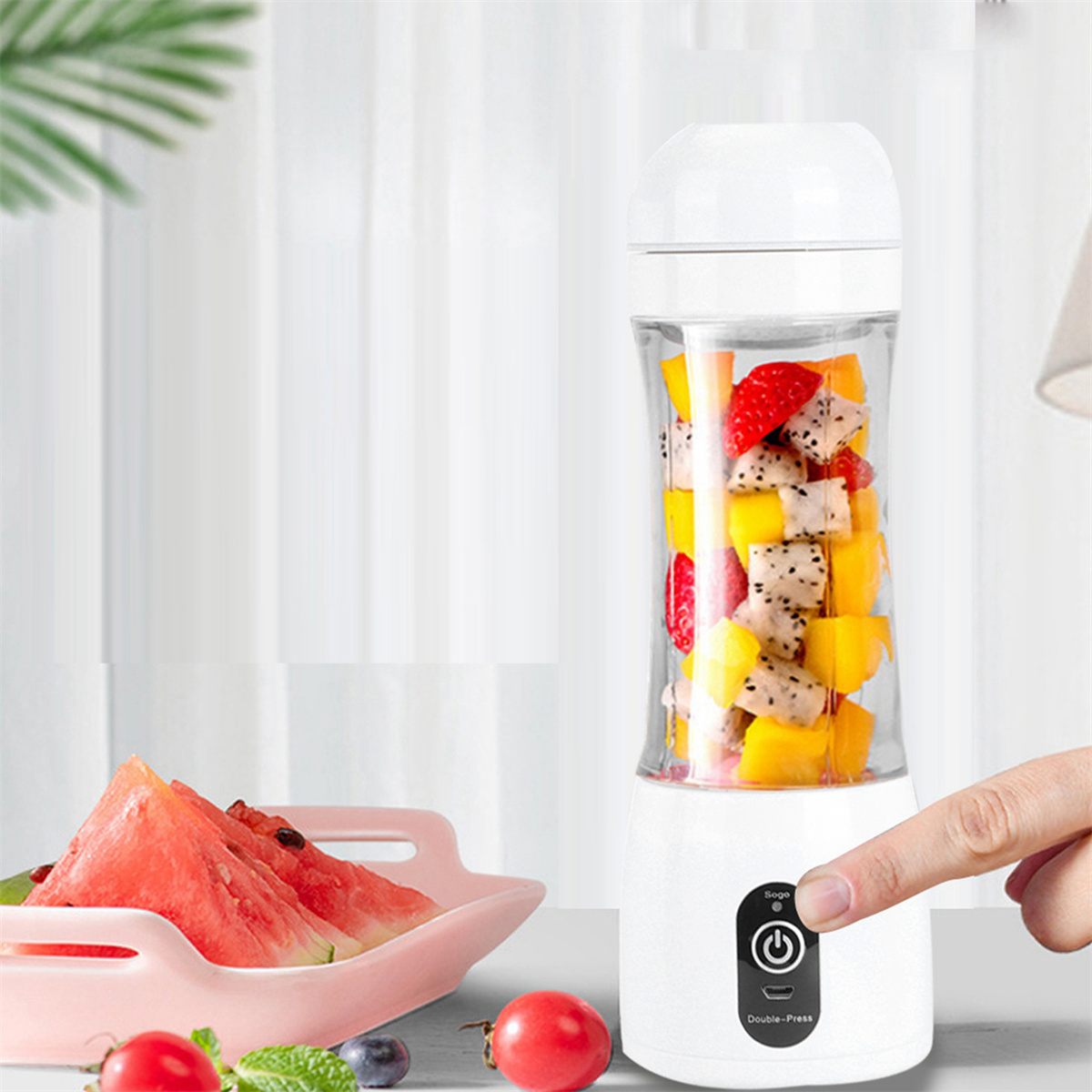 Ein Mixer mit Früchten, eine Hand drückt eine Taste. Wassermelone und Tomaten liegen daneben.