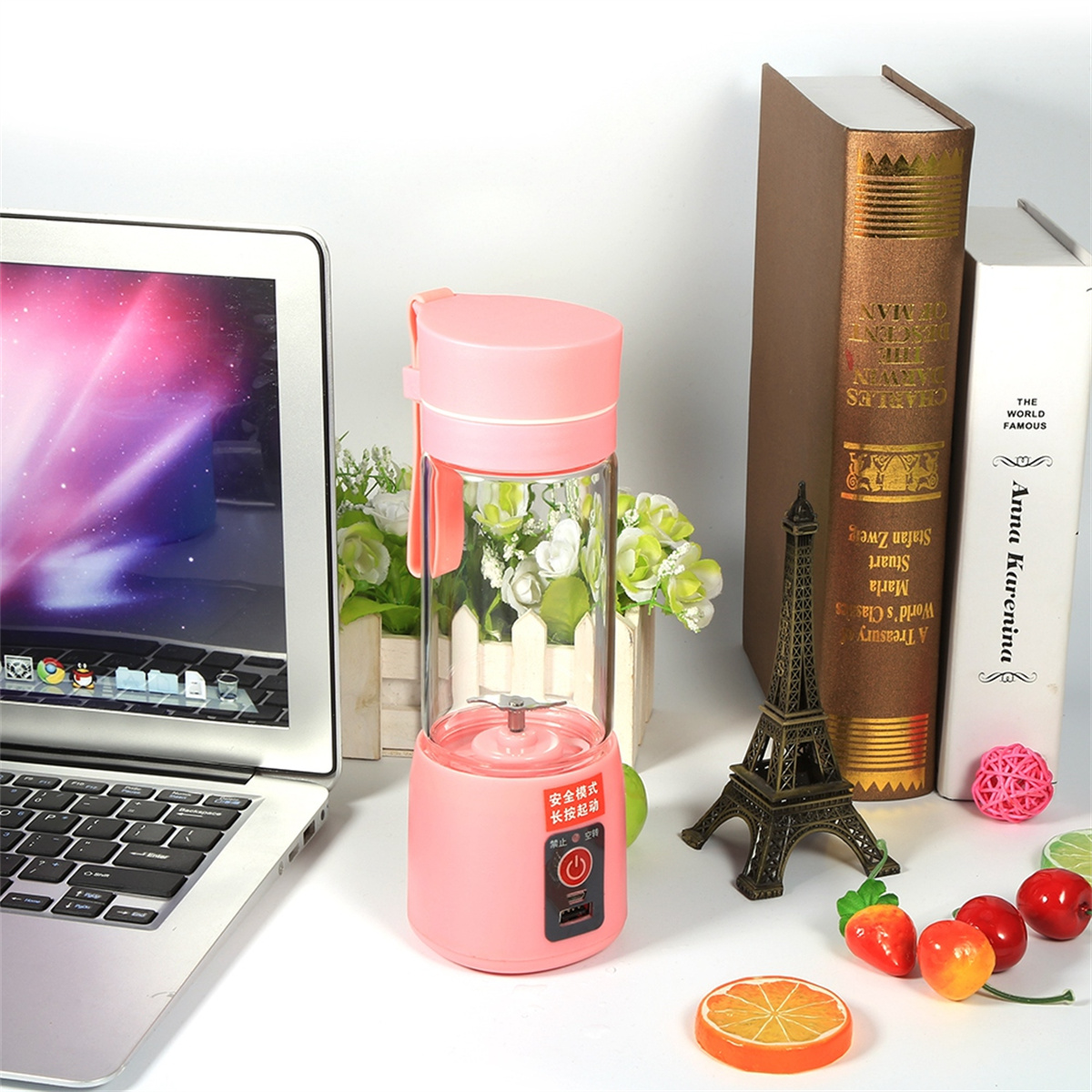 Rosa Blender mit rosa Deckel, steht auf einer weißen Oberfläche neben einem Laptop und etwas Kunstobst.