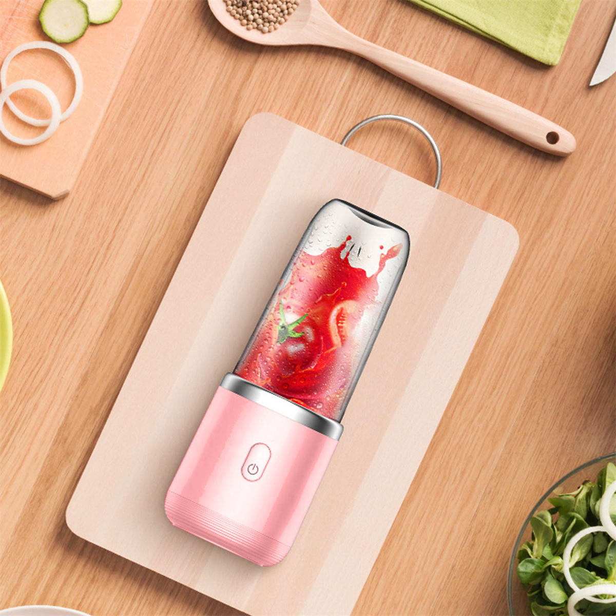 Rosa Mixer mit Erdbeeren auf einem Holzbrett. Gehackte Zwiebeln und Gurken liegen daneben.
