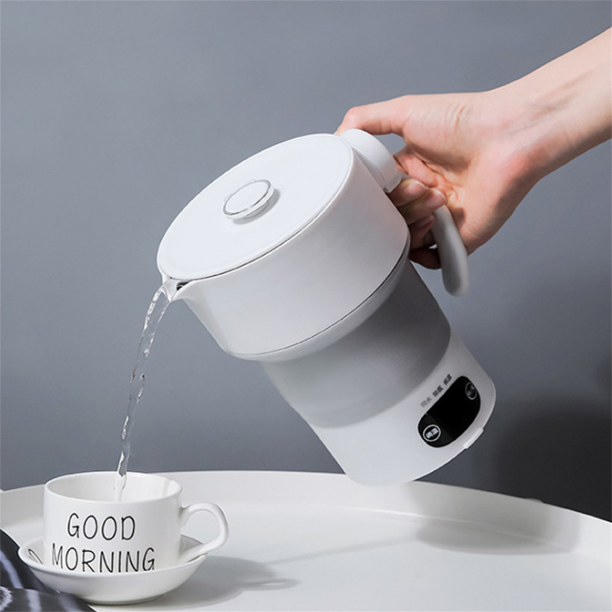 Ein weiß-grauer zusammenklappbarer Wasserkocher gießt Wasser in eine weiße Tasse.