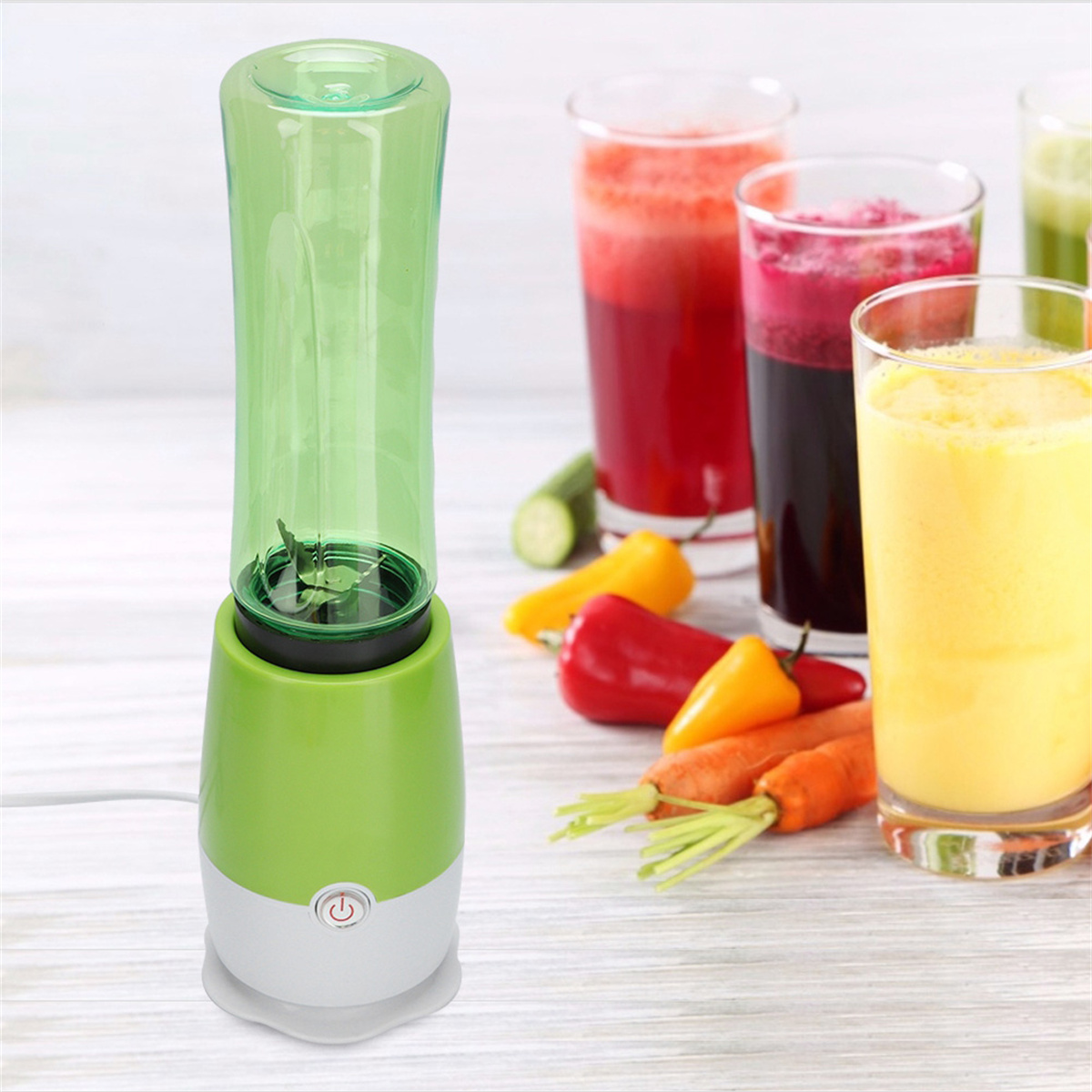 Grüner tragbarer Mixer mit Saftgläsern und Obst auf einem hellen Holztisch.