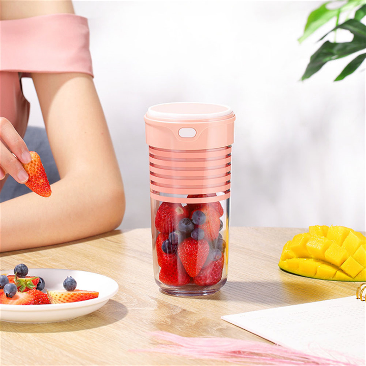Eine Frau mit einer Erdbeere und ein Mixer mit Erdbeeren und Blaubeeren darin.