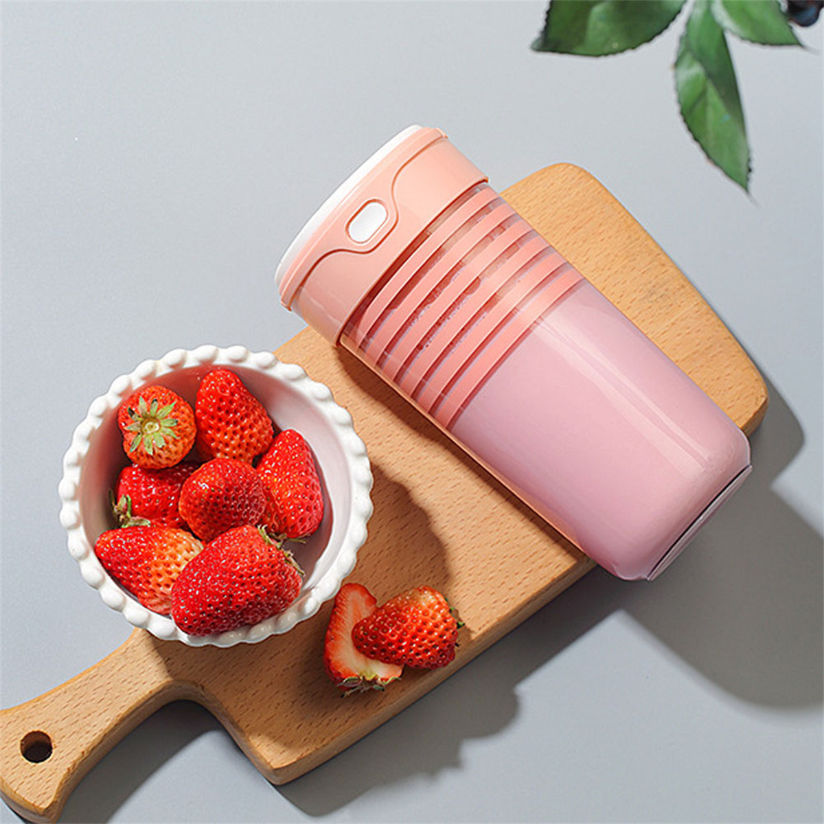 Ein rosa Mixer mit Erdbeeren in einer Schüssel auf einem Holzbrett. Der Mixer ist teilweise gefüllt.