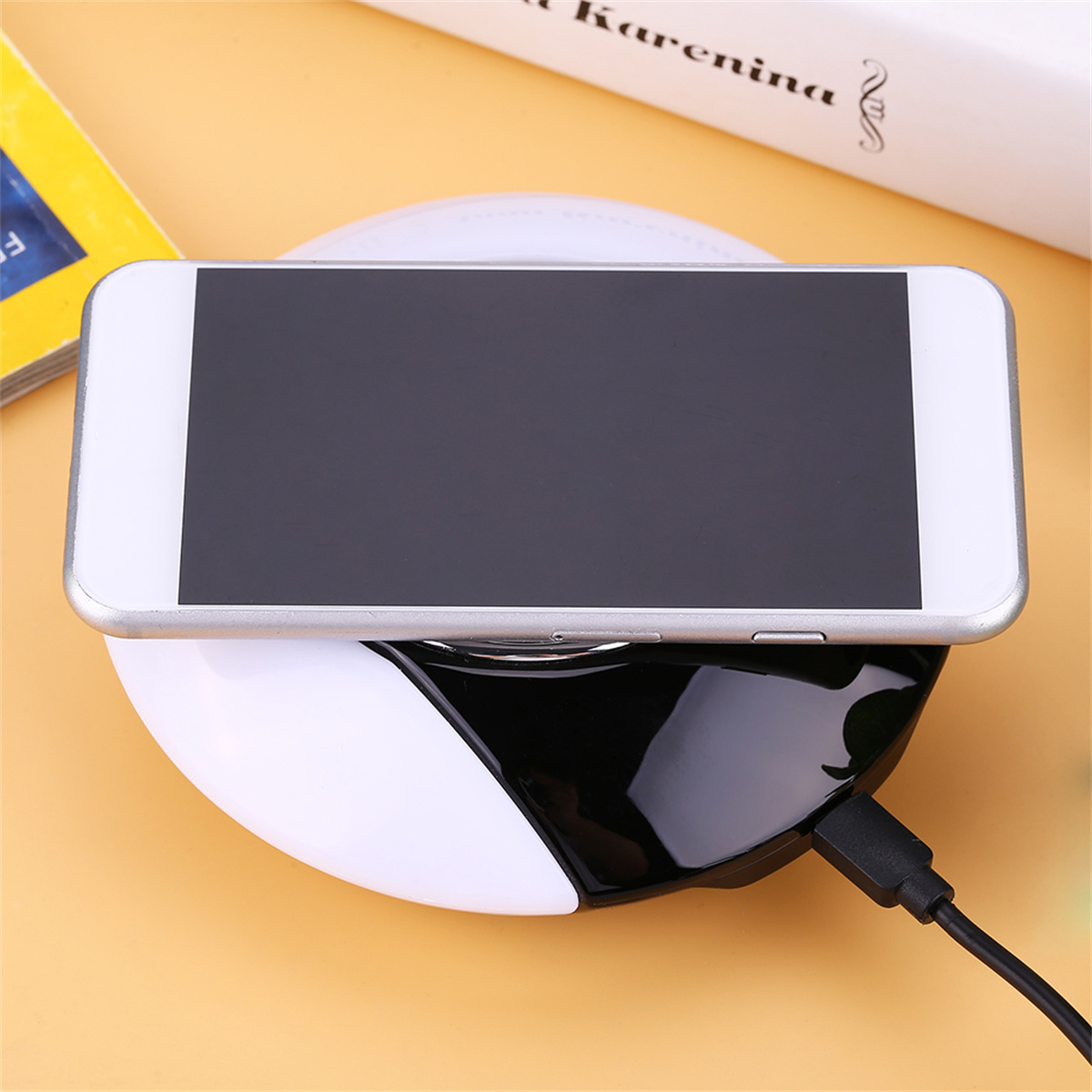 Weißes Telefon auf einem schwarz-weißen Ladegerät. Ein schwarzes Kabel ist angeschlossen. Bücher sind im Hintergrund.